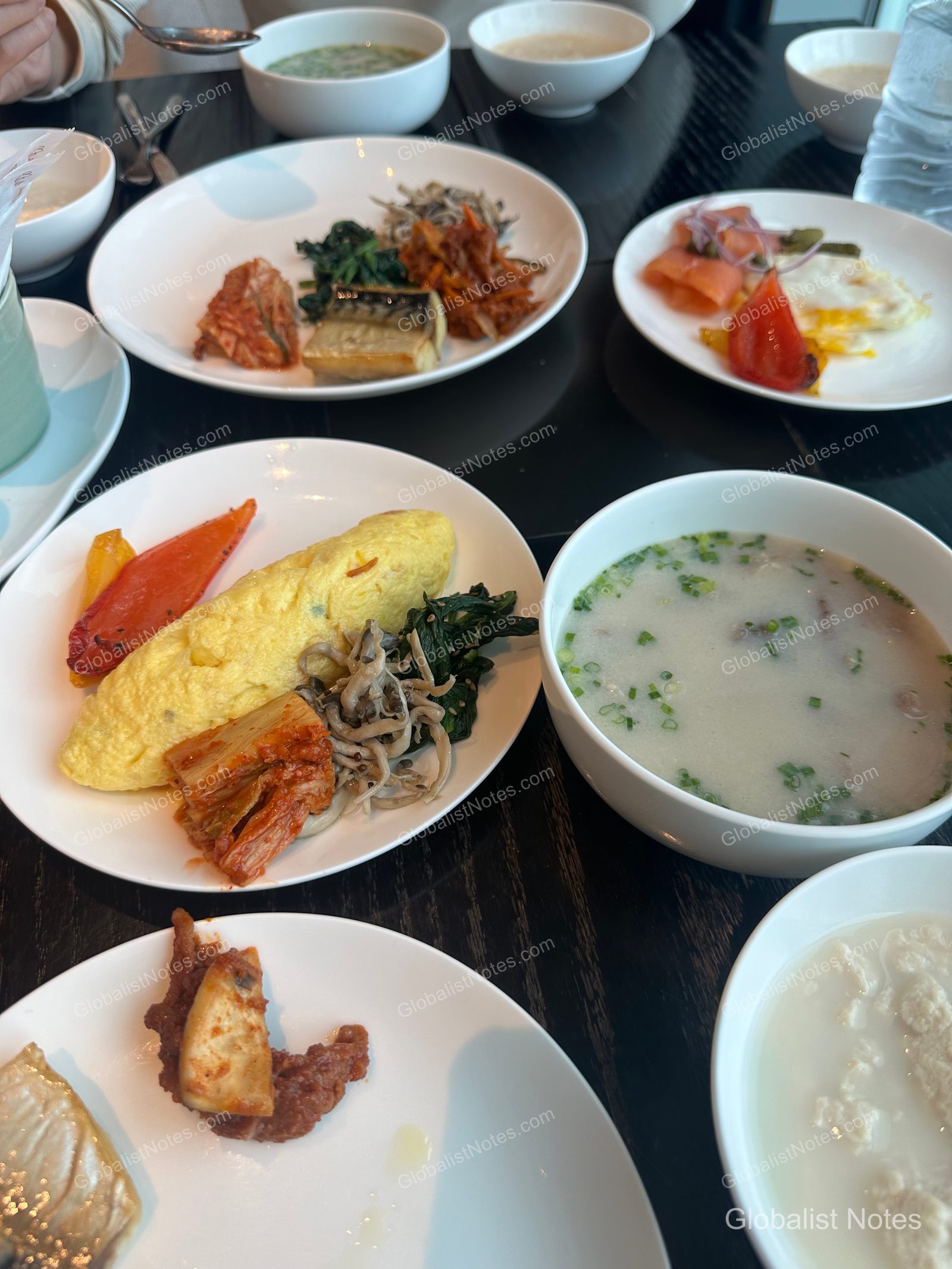 A breakfast buffet table at Grand Hyatt Jeju featuring a mix of Korean and Western dishes, including an omelet, roasted vegetables, kimchi, namul, grilled fish, and a bowl of warm soup.