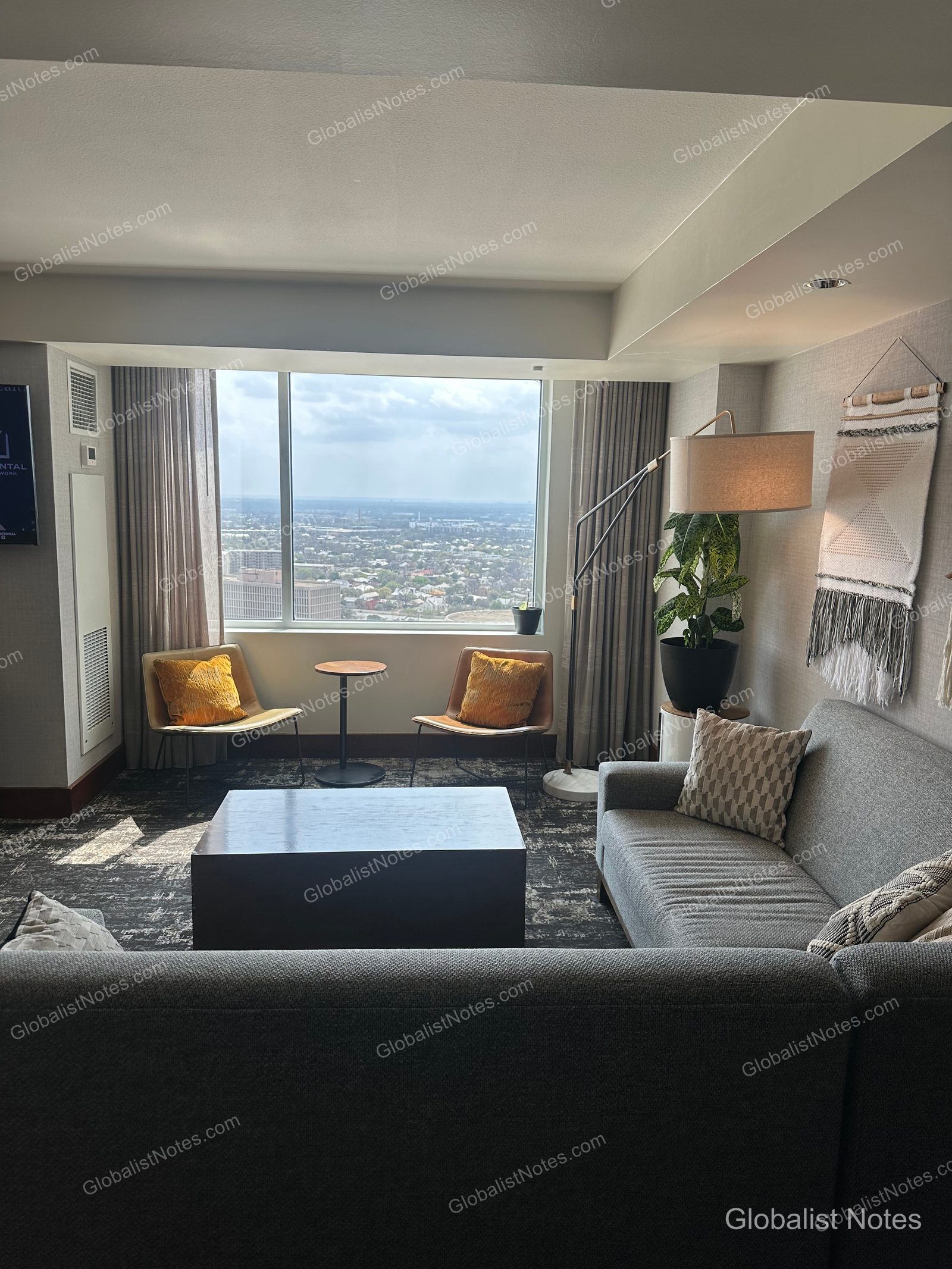 The living area of an Executive Suite at Grand Hyatt San Antonio River Walk, featuring a gray sofa, two chairs with yellow cushions, and a small round table by the window overlooking the city.