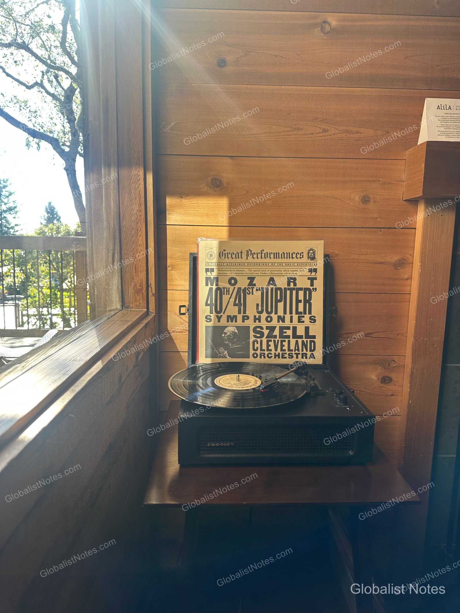 A Crosley turntable and a Mozart LP record placed against a wood-paneled wall in an Alila Ventana Big Sur Junior Suite, with sunlight streaming in and a view of the forest outside.