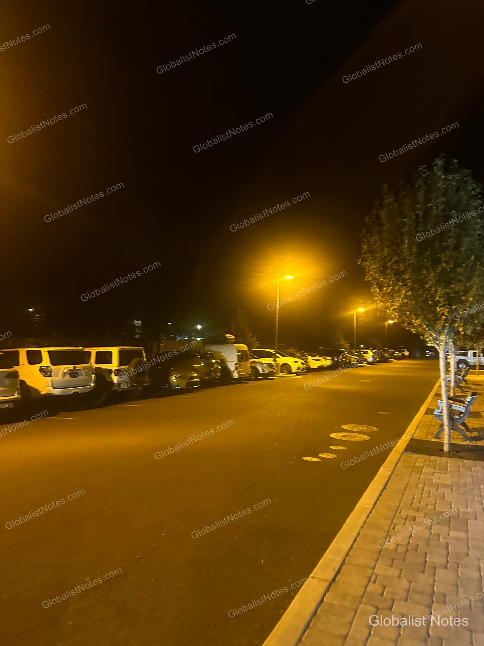 夜のHyatt Place Flagstaffの屋外駐車場。街灯に照らされた車が並び、右手に歩道と木製のベンチが見えます。