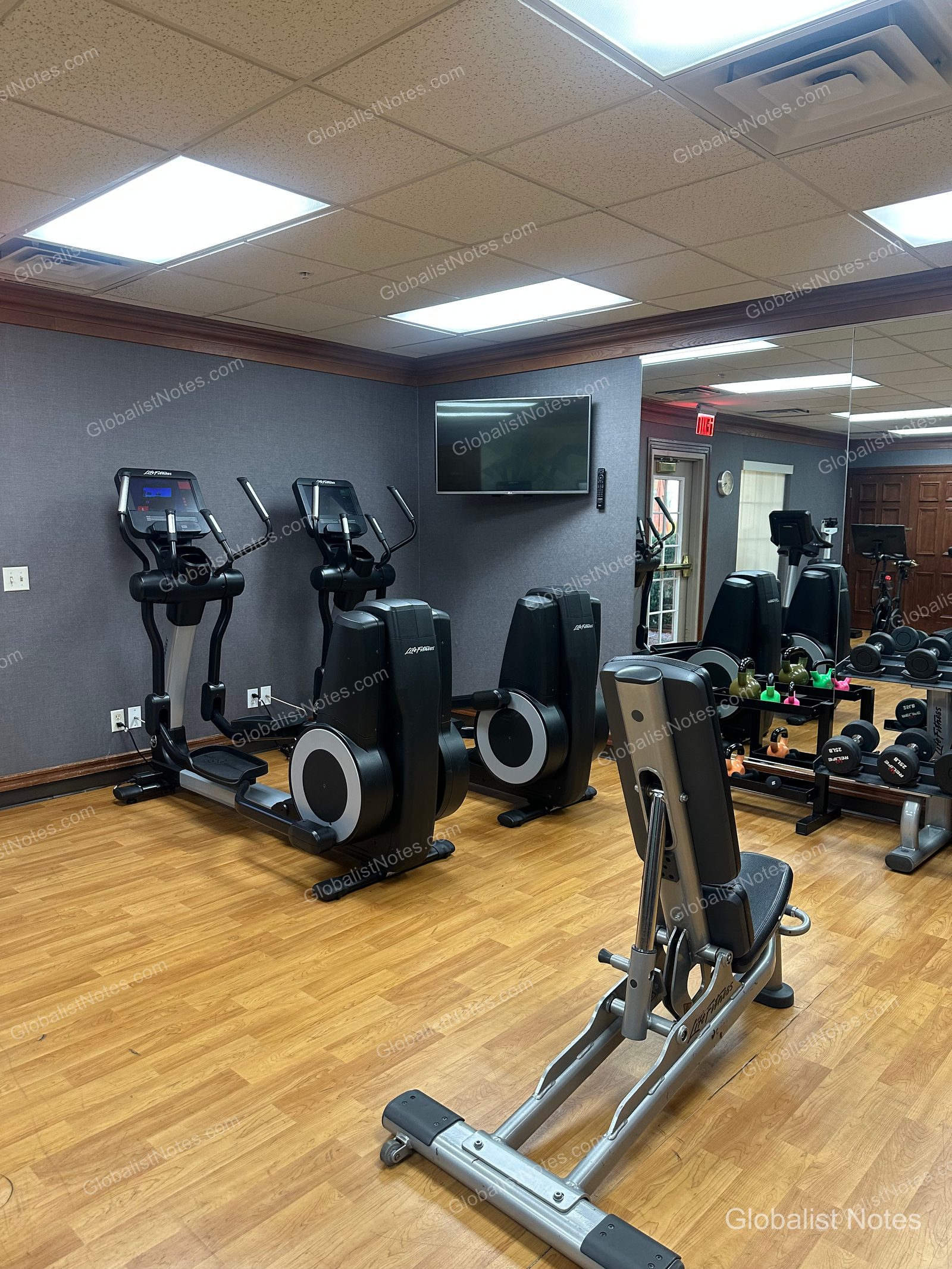 Hyatt House Scottsdale/Old Townのフィットネスセンター。木目調の床にLife Fitness製のエリプティカルマシン2台、ベンチ、鏡の前にはダンベルやケトルベルなどのトレーニング機器が並んでいます。