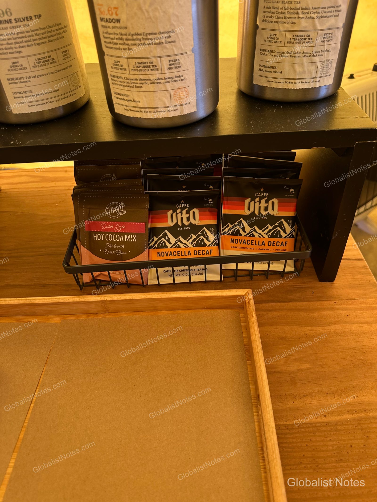 Under Canvas North Yellowstoneのテント内。木製テーブルの上に、Smith Teamakerのティー缶3つと、Caffe Vitaのホットココアやデカフェコーヒーが入った黒いアイアンバスケットが置かれています。