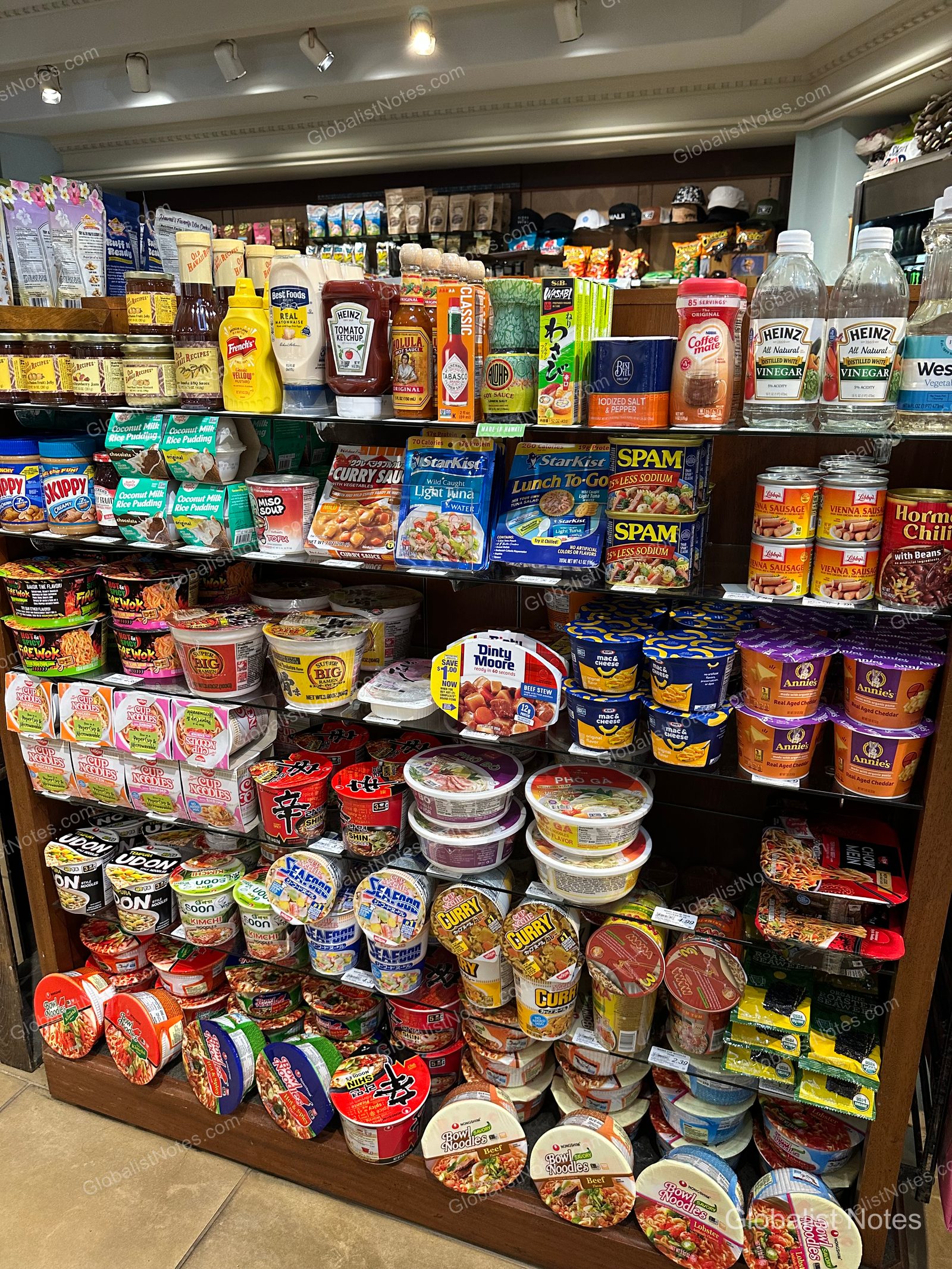 Shelves stocked with various groceries at the shop inside Hyatt Regency Maui Resort and Spa. The top shelves feature sauces and vinegars, while the middle and lower shelves are packed with instant noodles, Spam, instant rice, and mac and cheese.