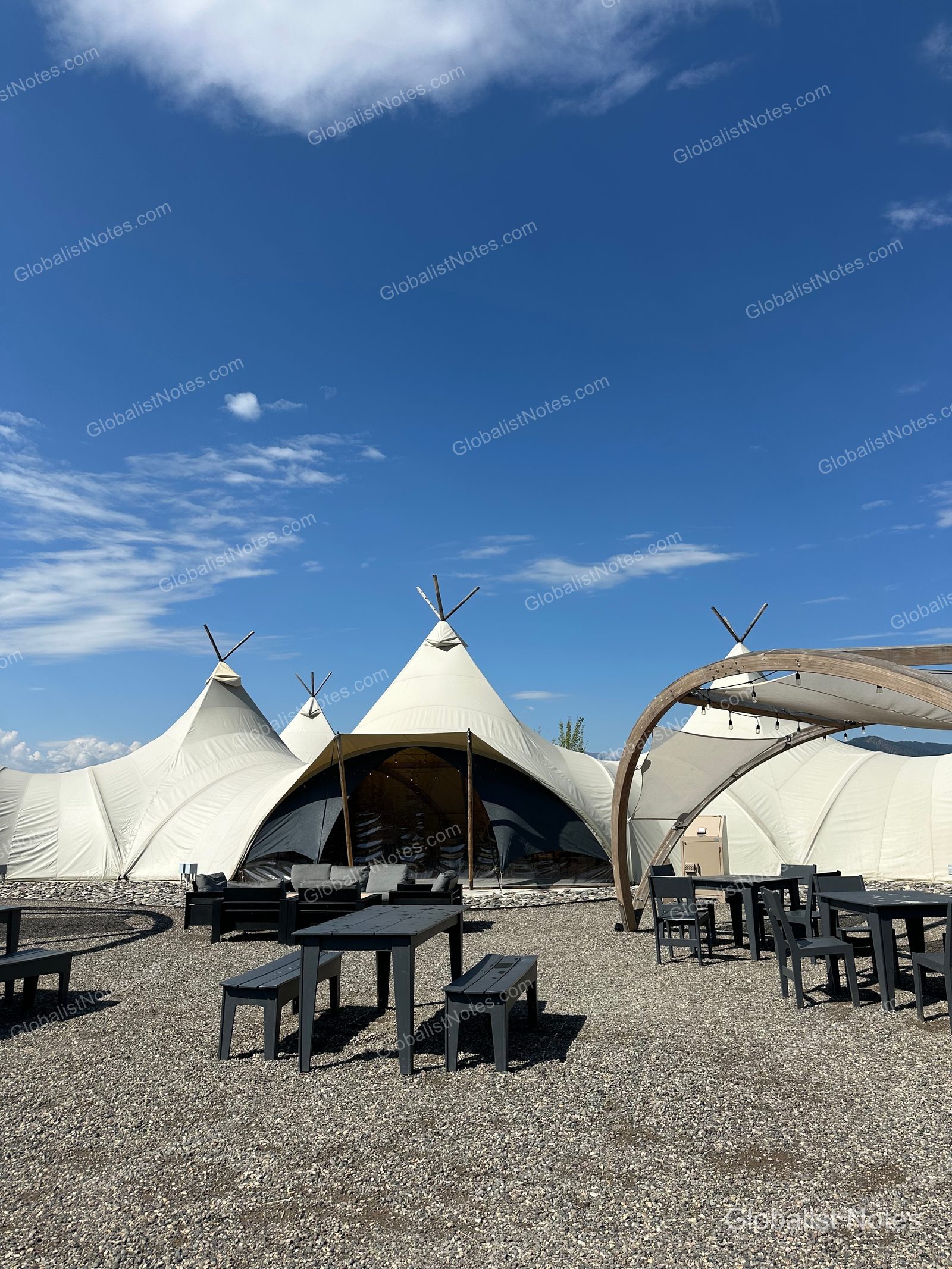 Under Canvas North Yellowstoneの全景。砂利敷きのエリアに大型のホワイトキャンバステントが並び、黒いテーブルと椅子が配された開放的な空間。
