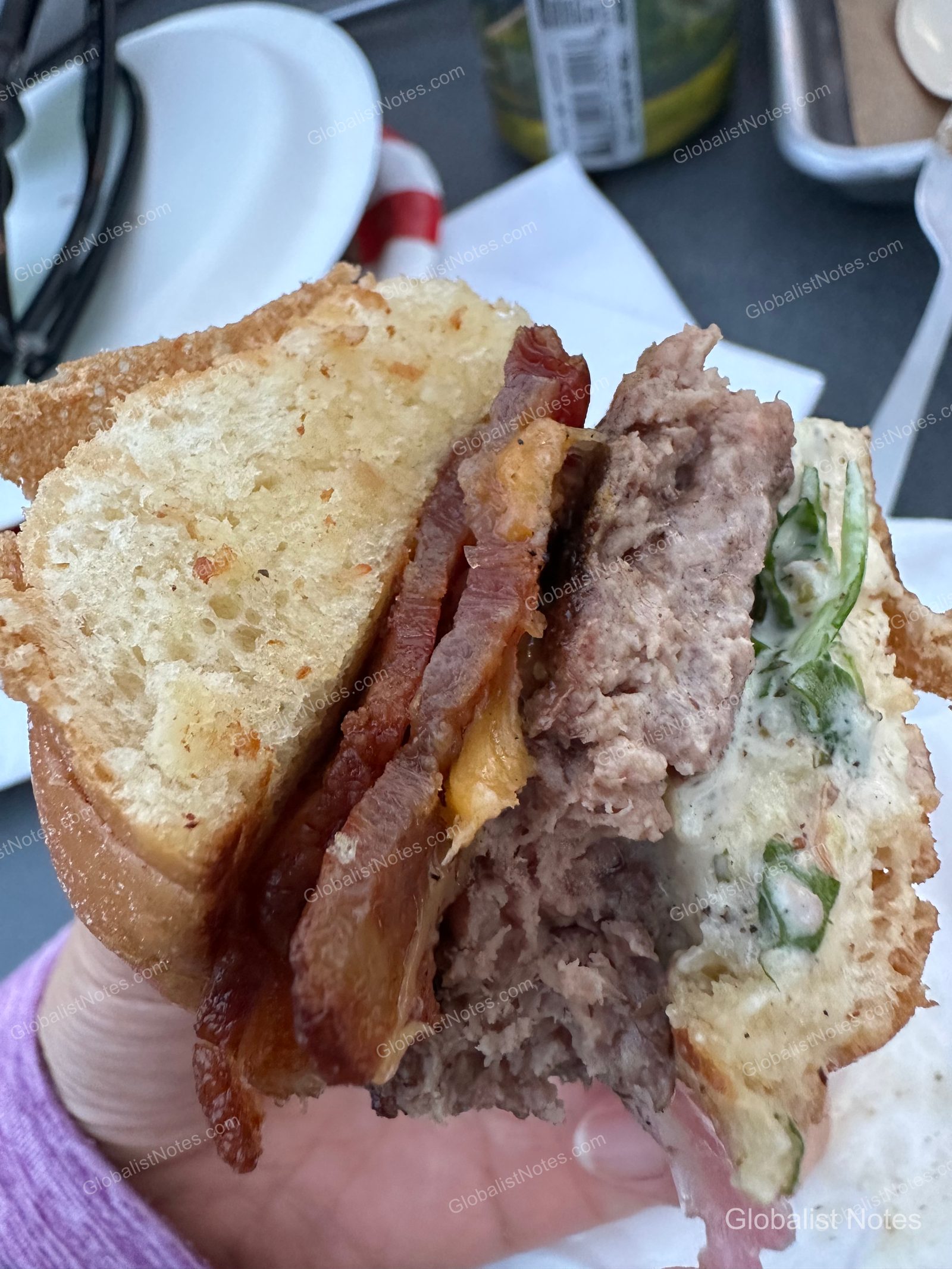 ハンバーガーの断面。焼いたバンズの間に厚みのあるパティ、ベーコン、とろけたチーズ、そしてたっぷりの野菜が層になっています。