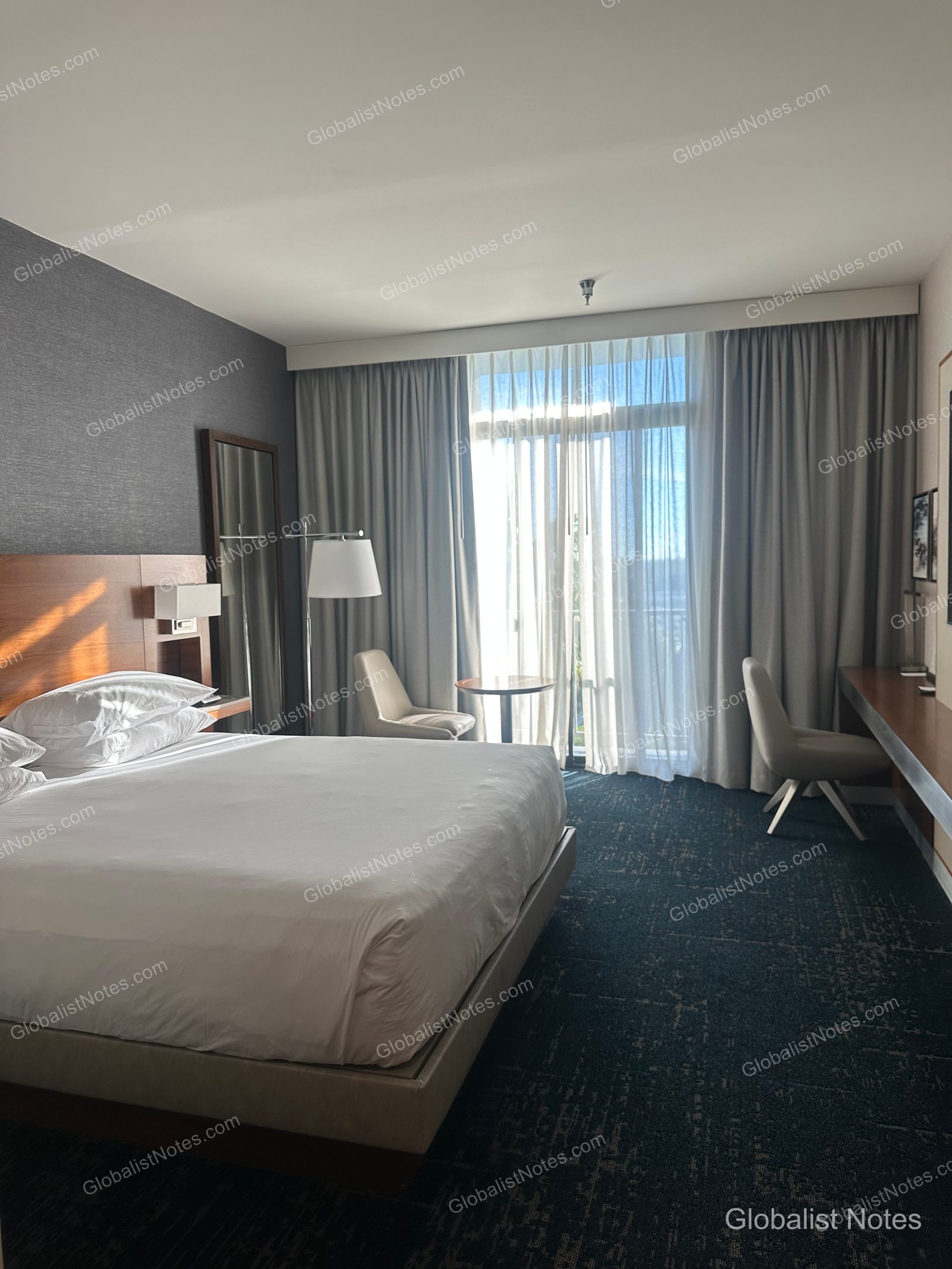 Newport Beach Hyatt Regency 標準大床房內部，配有白色寢具的大床、窗邊桌椅及長型辦公桌，自然光透過窗簾灑入室內。