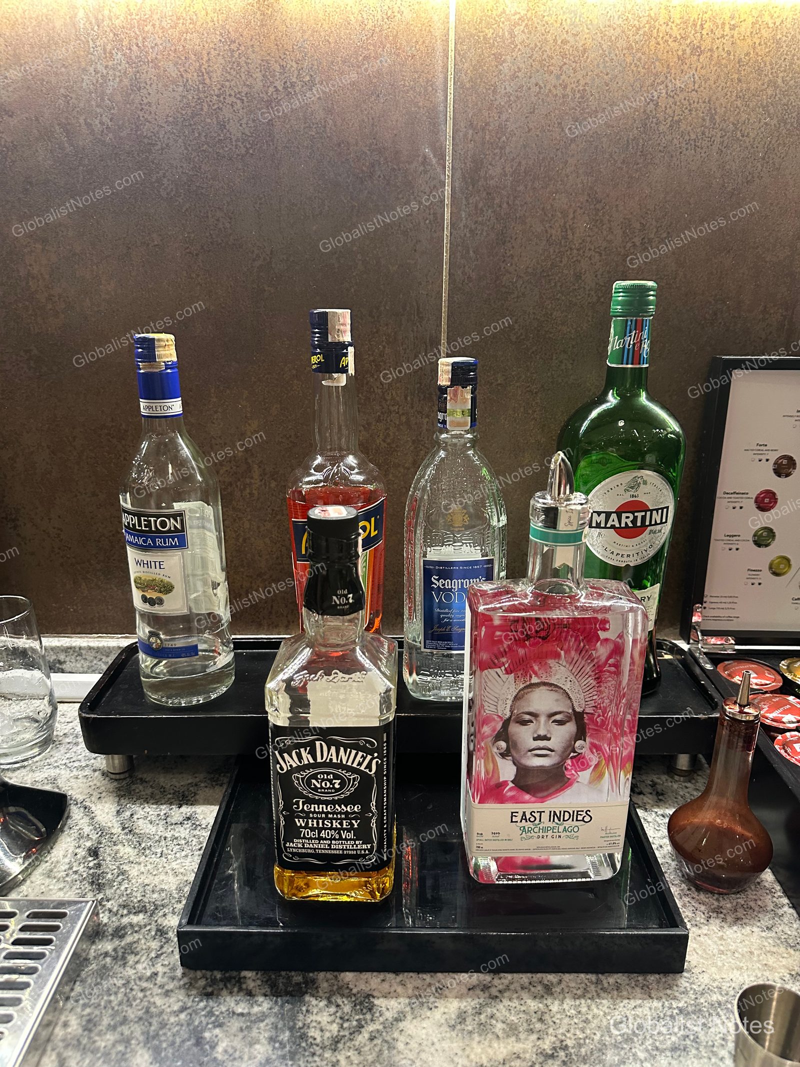 A selection of spirits at the Grand Hyatt Jakarta lounge, featuring bottles such as Appleton Rum, Jack Daniel's whiskey, Seagram's vodka, Martini vermouth, and East Indies gin arranged on a black tray.