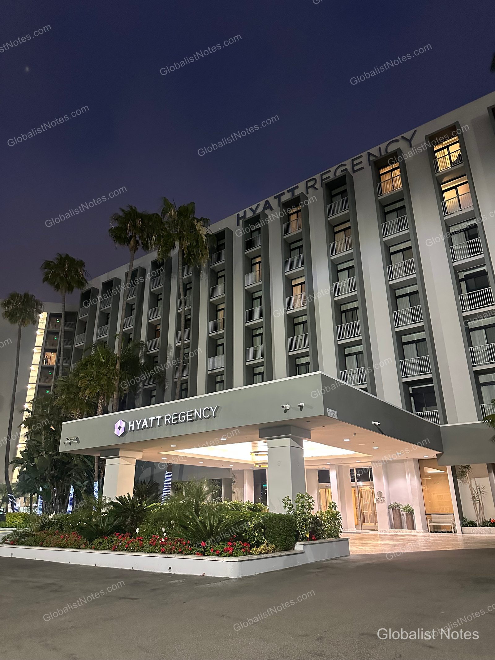 Hyatt Regency Newport Beach West 外觀，黃昏燈光下顯得明亮。現代化多層建築與入口雨遮，搭配周邊棕櫚樹與景觀造景。