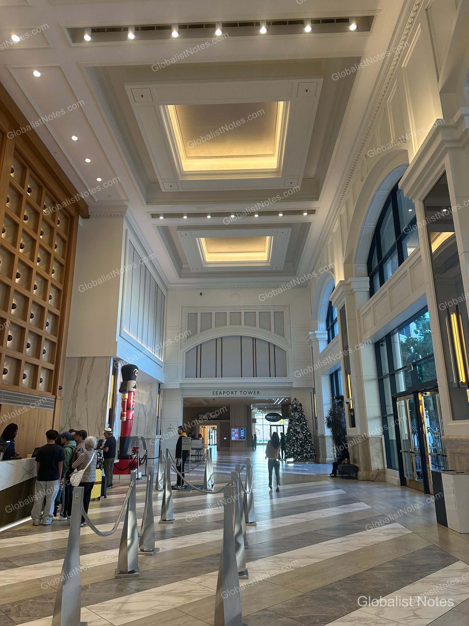 Manchester Grand Hyatt San Diego 挑高大廳，地面鋪設大理石。左側為接待櫃檯，中央通道盡頭可見 Seaport Tower 指示牌與聖誕樹。