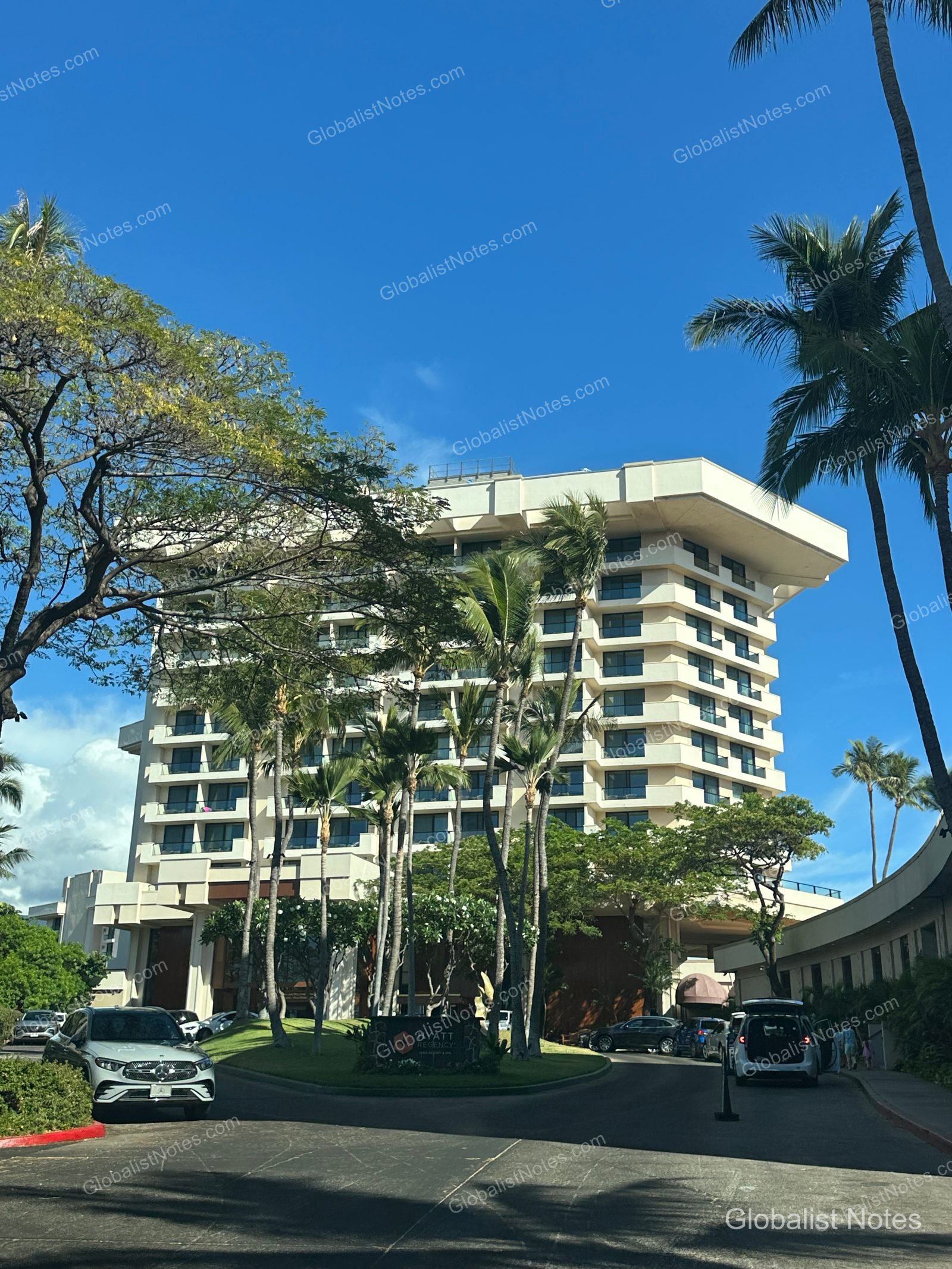 Exterior view of Hyatt Regency Maui Resort and Spa in Lahaina, Hawaii, showing the multi-story hotel building under a blue sky with palm trees and parked cars near the entrance.