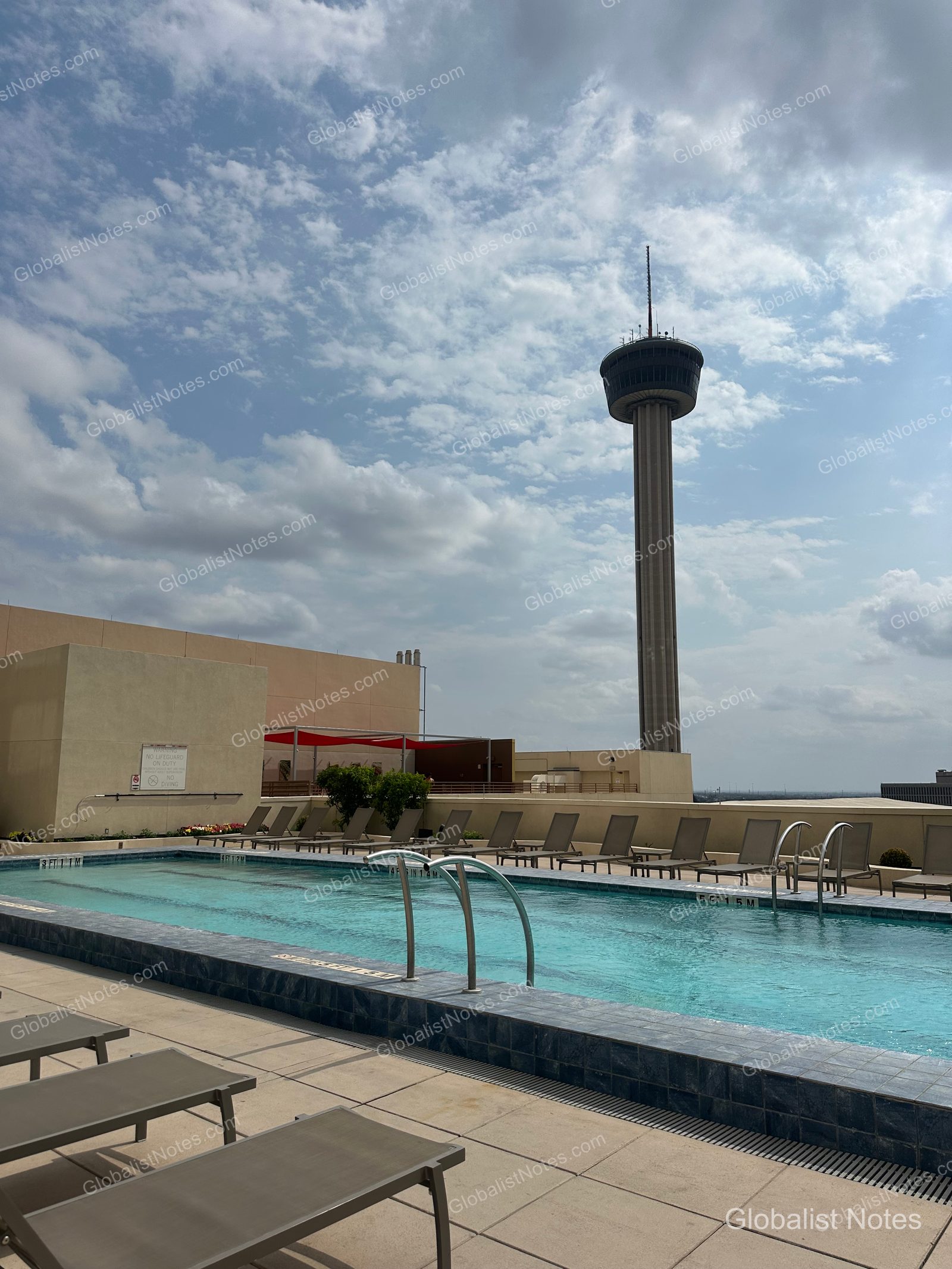 The rooftop outdoor pool at Grand Hyatt San Antonio River Walk. The rectangular blue-tiled pool is surrounded by sun loungers, with the Tower of the Americas rising prominently in the background.