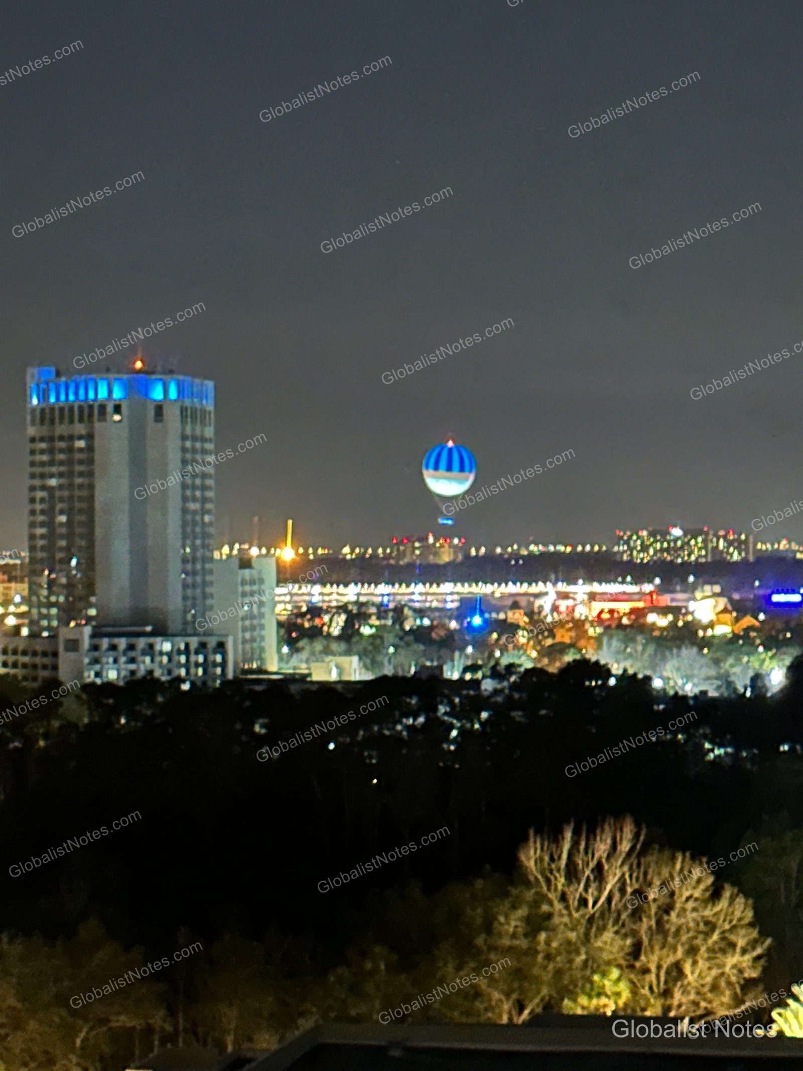 Night view from a guest room at Hyatt Regency Grand Cypress, featuring a distant high-rise building with blue lighting and a hot air balloon against the dark night sky.