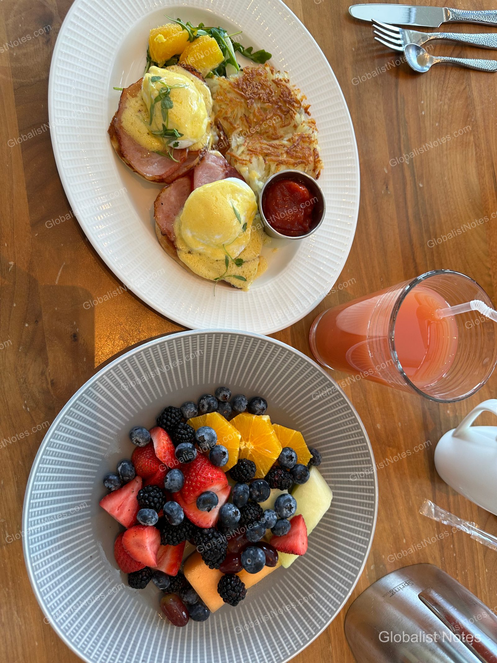 Breakfast at Hyatt Regency Grand Cypress in Orlando, featuring Eggs Benedict, hash browns, a bowl of fresh fruit, and red juice on a wooden table.
