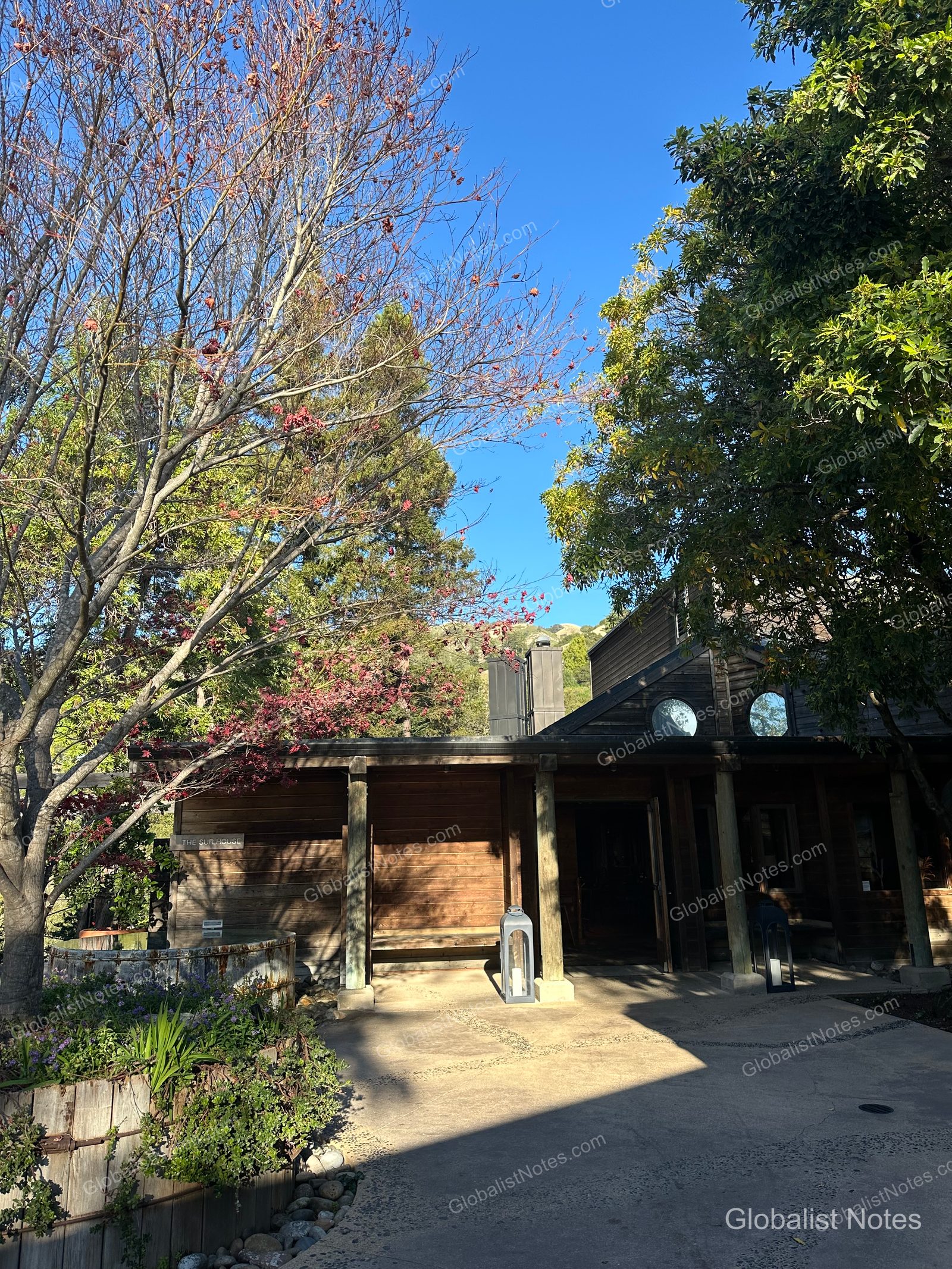 The exterior of The Sur House at Alila Ventana Big Sur under a clear sky, surrounded by trees and gardens with lanterns placed at the entrance.