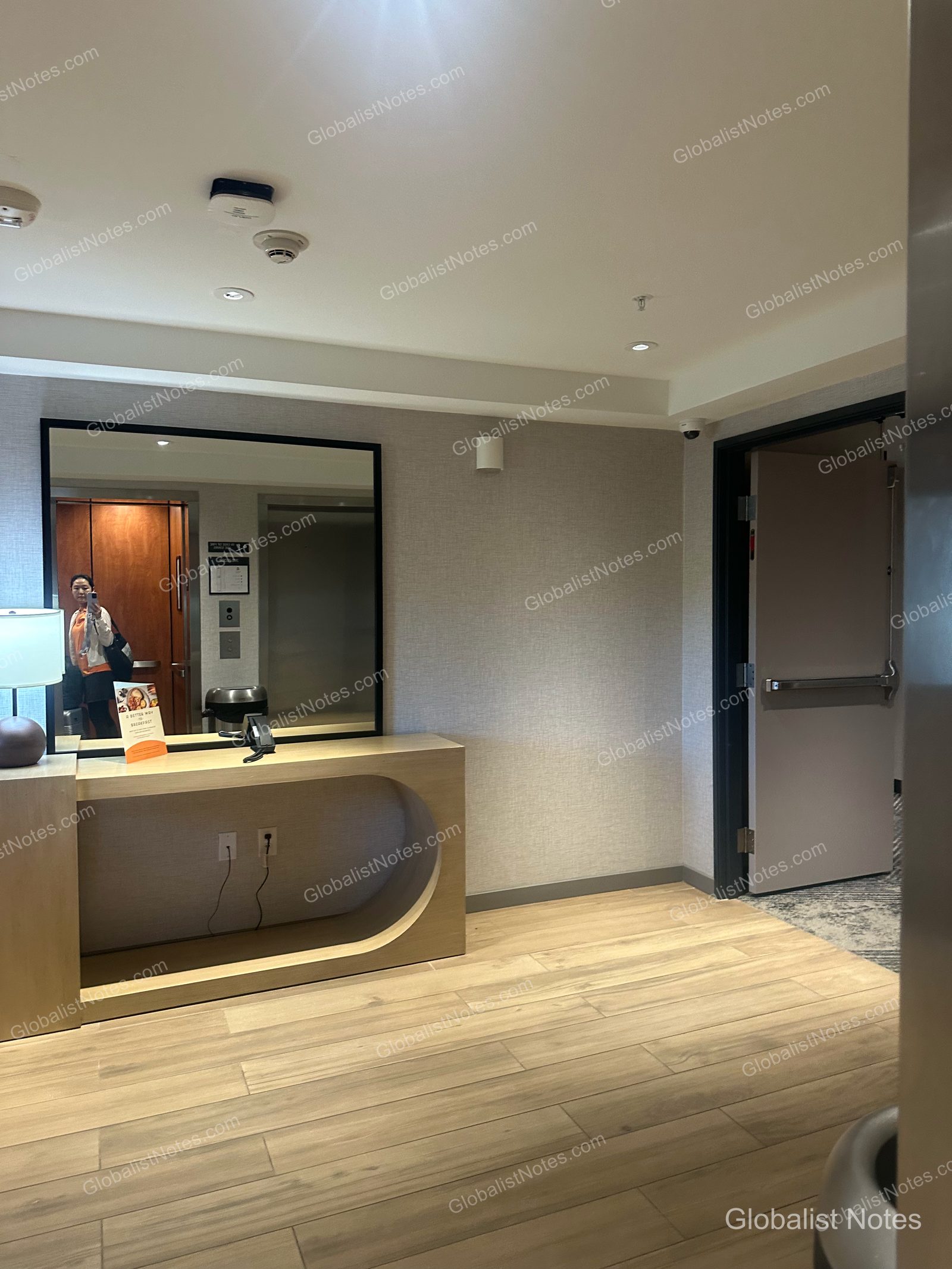 Hyatt Place Flagstaffの廊下。明るい木目調のコンソールテーブルと大きな鏡が置かれています。右側には客室ドアが並び、床は木目調の仕上げです。