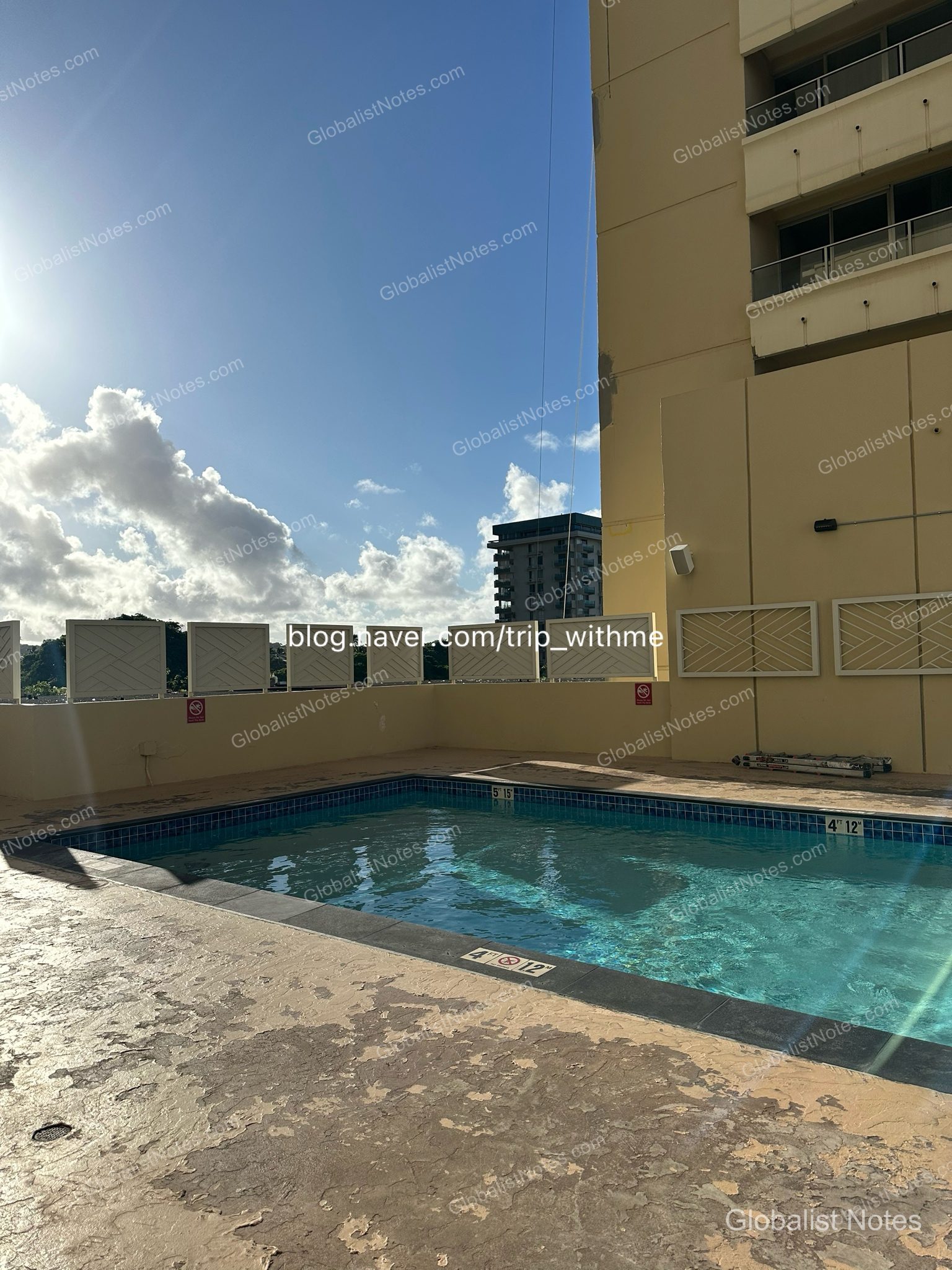 Outdoor pool at Hyatt Place Waikiki Beach in Honolulu, Hawaii. The rectangular pool is under a blue sky, enclosed by beige walls and low fencing, with some visible wear on the pool deck.