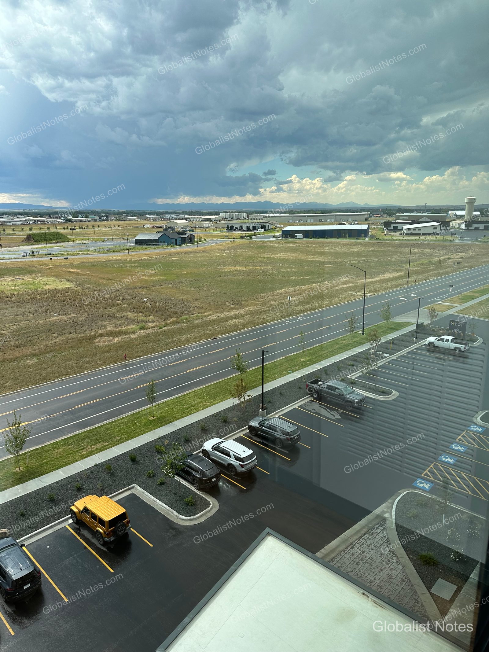 Hyatt Place Bozeman Yellowstone Airportの客室から見下ろした、曇り空と平原、そしてホテルの駐車場。