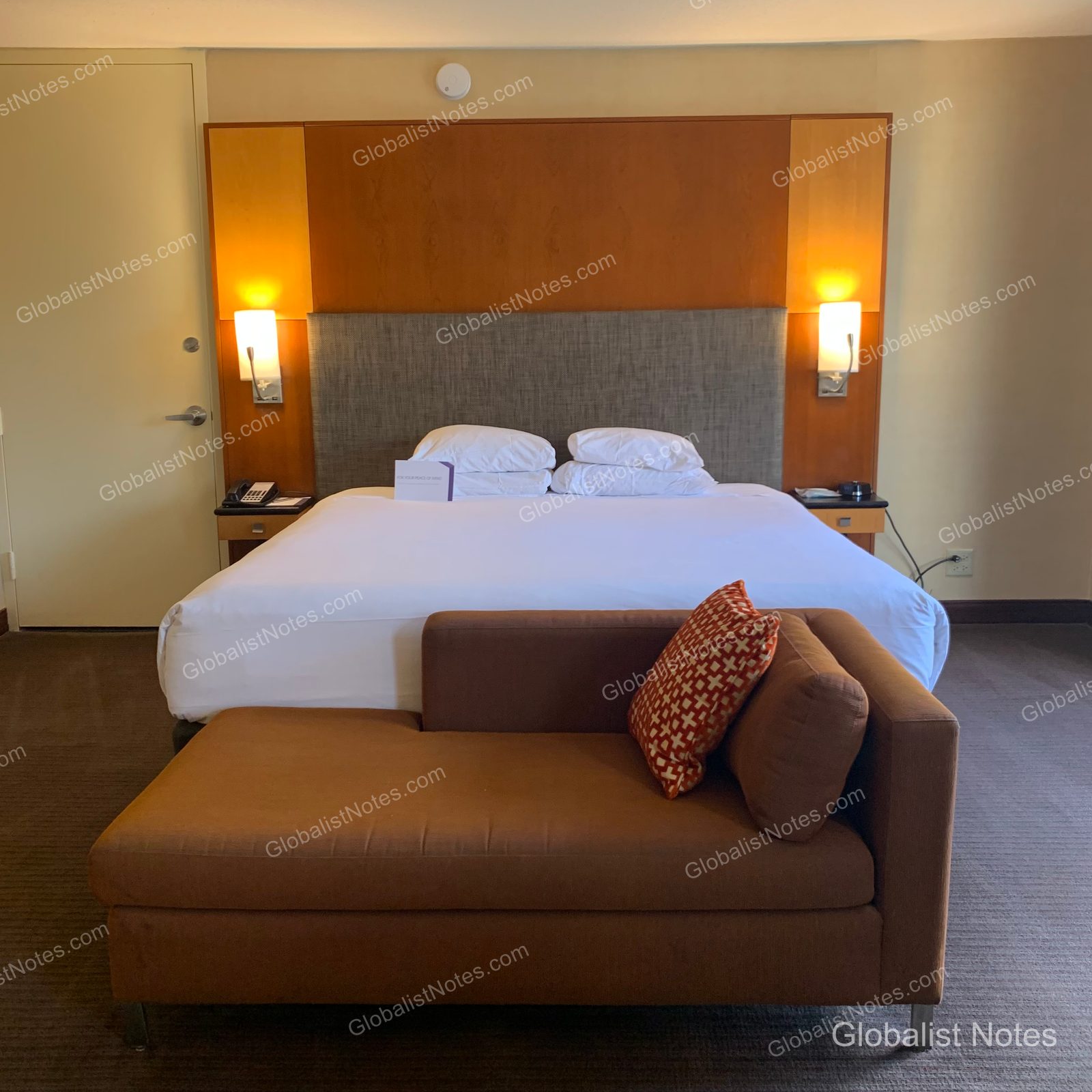 Hyatt Regency Chicagoのジュニアスイートルーム。中央にキングベッド、手前にブラウンのデイベッドが配されています。ベッドの両サイドには照明付きの木製ヘッドボードがあり、ベッド上には案内カードが置かれています。