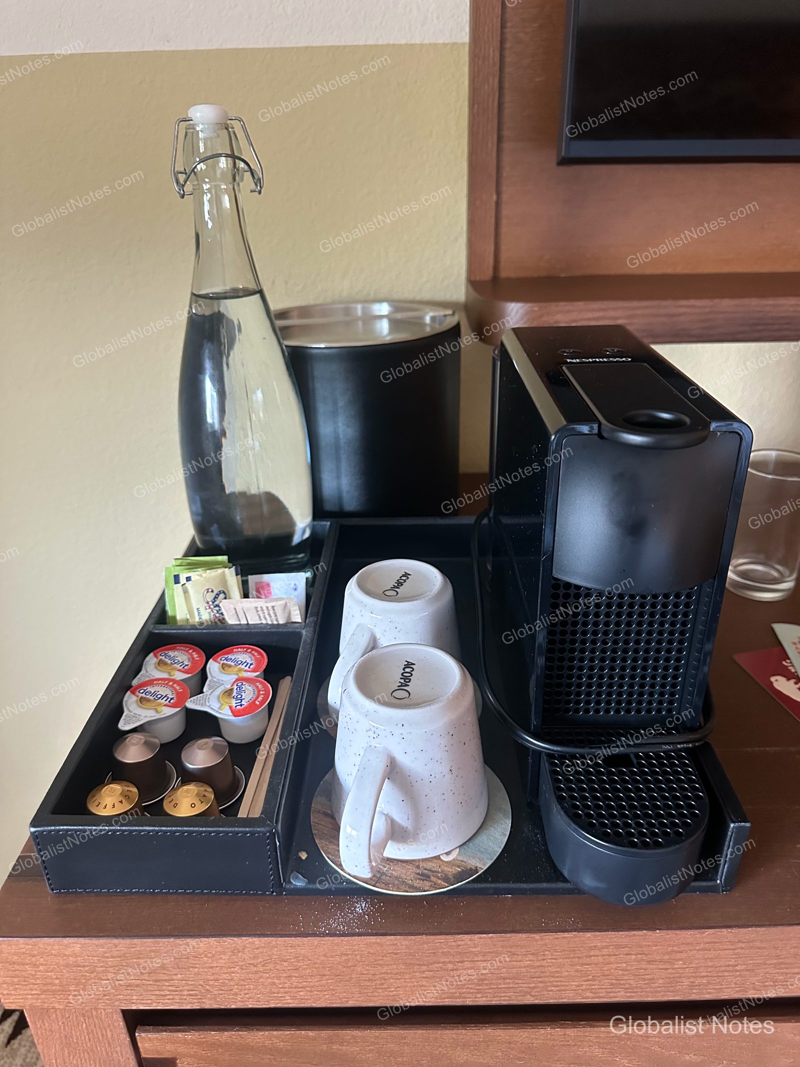 ボーズマンのWandering Buffaloの客室にあるコーヒーコーナー。黒いネスプレッソマシン、ガラス製ウォーターボトル、アイスペール、コーヒーカプセル、クリーマー、マグカップ2つがトレイの上に整然と並んでいます。