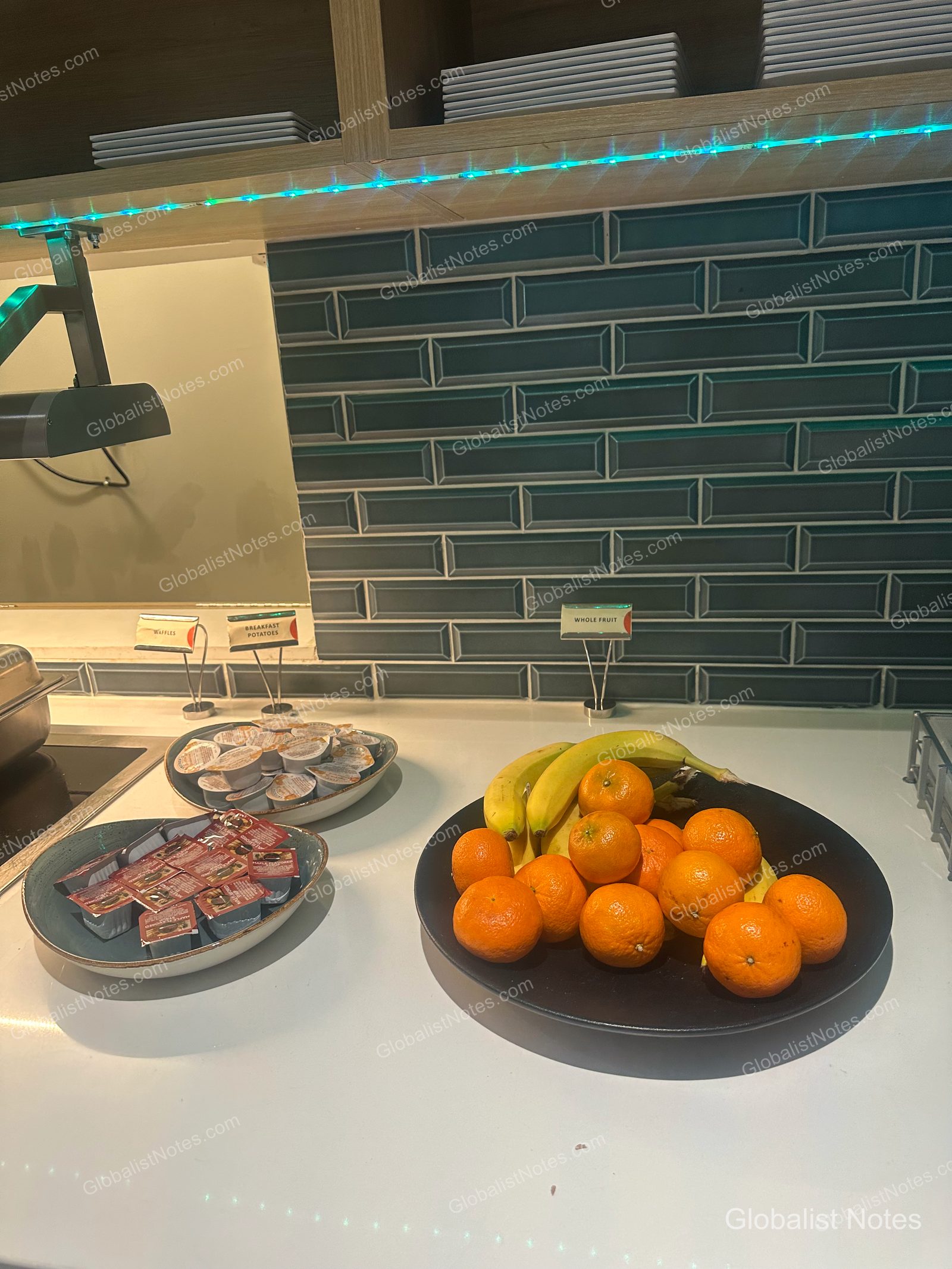 Hyatt Place Flagstaffの朝食コーナー。白いカウンターにフルーツが盛られた皿と、ワッフルやポテト用のソース類が並ぶ。背景はダークターコイズのタイル壁。