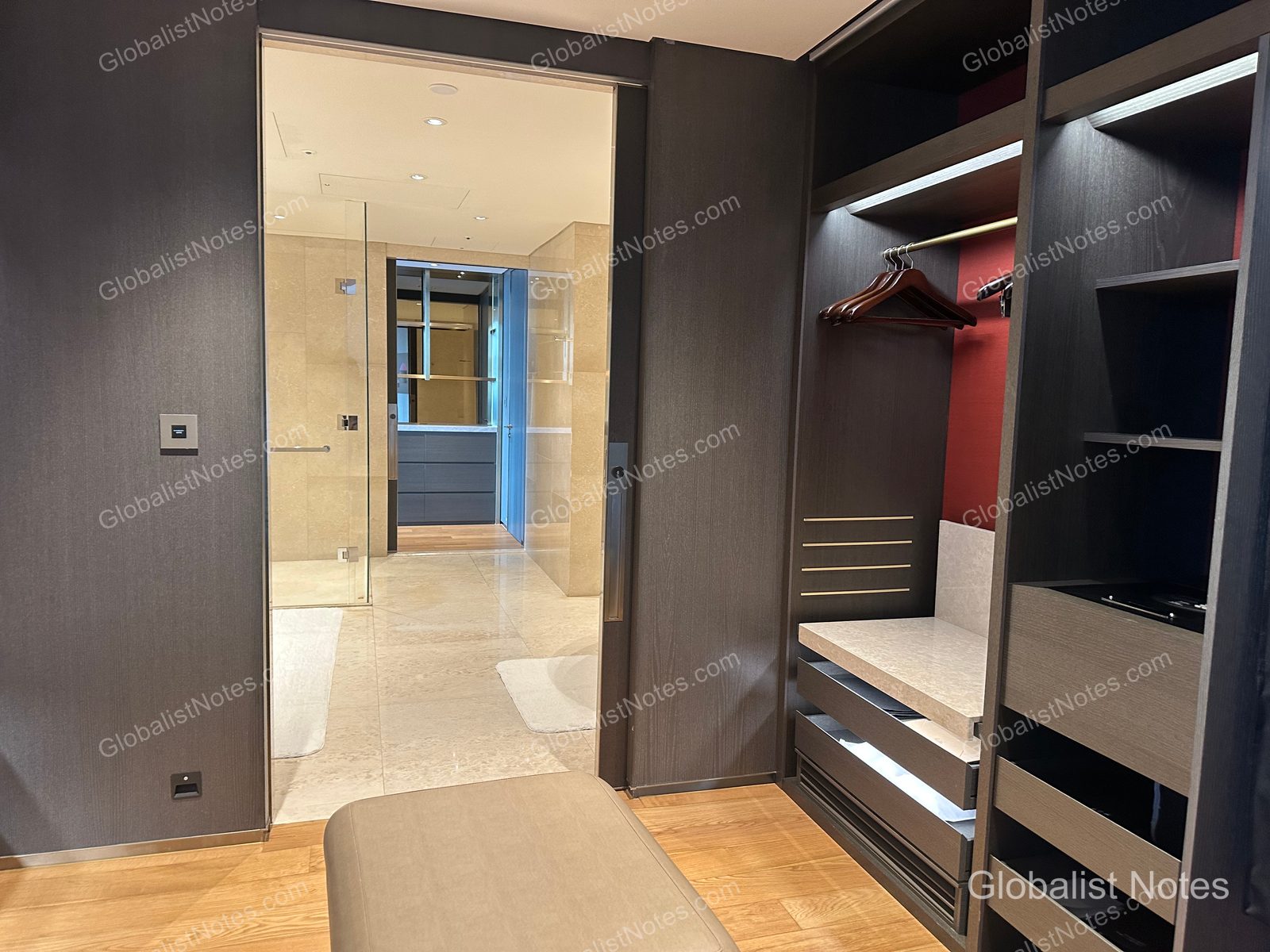 Inside the walk-in closet of a One Bedroom Suite at Grand Hyatt Jeju. It features dark-toned built-in wardrobes and hangers, with a view through the sliding door into the bright, marble-finished bathroom.