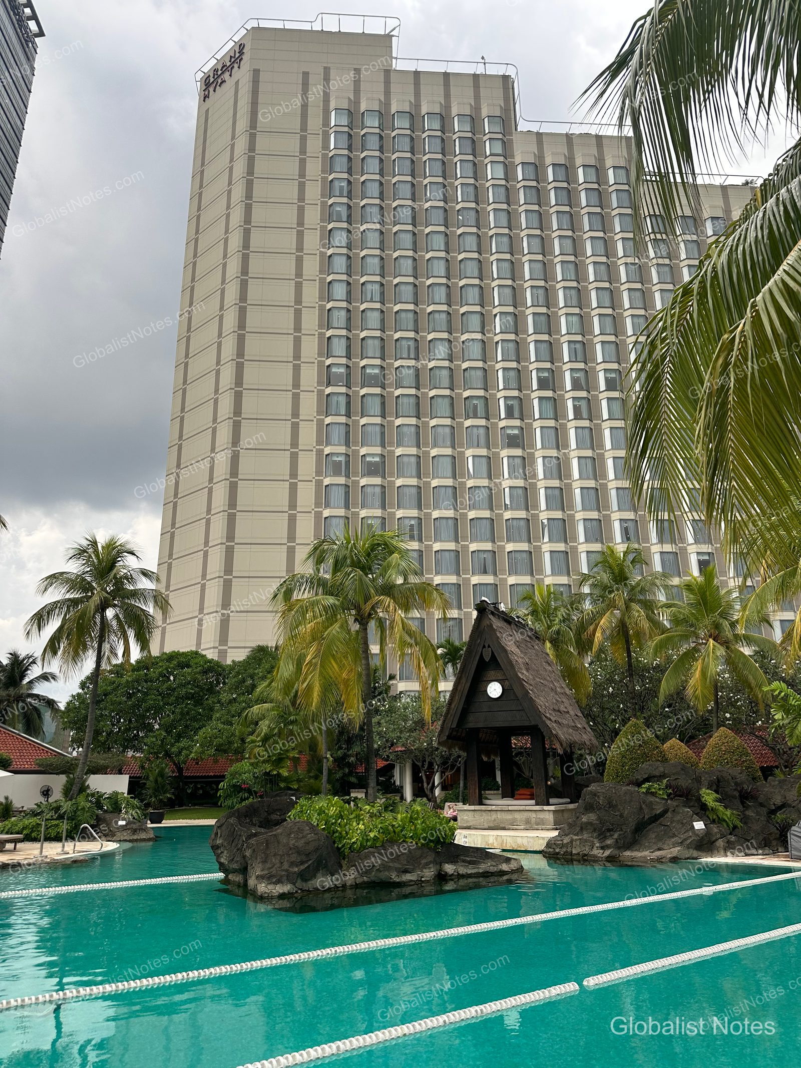 The exterior of the Grand Hyatt Jakarta, a high-rise building in the city center, with the outdoor pool and tropical landscaping visible in the foreground.