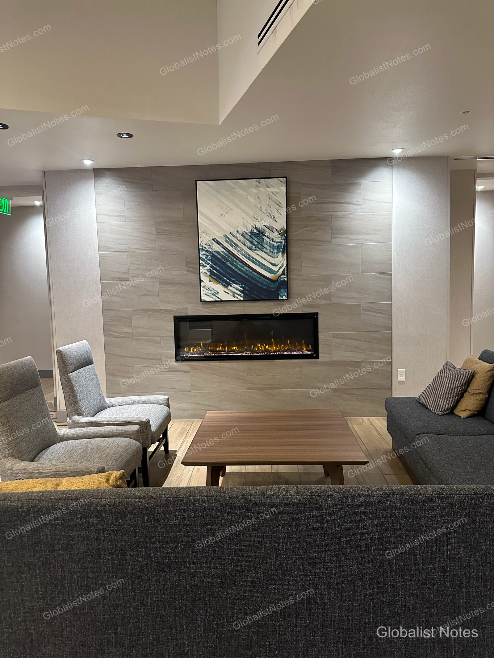 Hyatt Place Flagstaffのロビー。壁には埋め込み式の暖炉と抽象画があり、手前には木製のローテーブルとグレーのソファ、椅子が配されています。