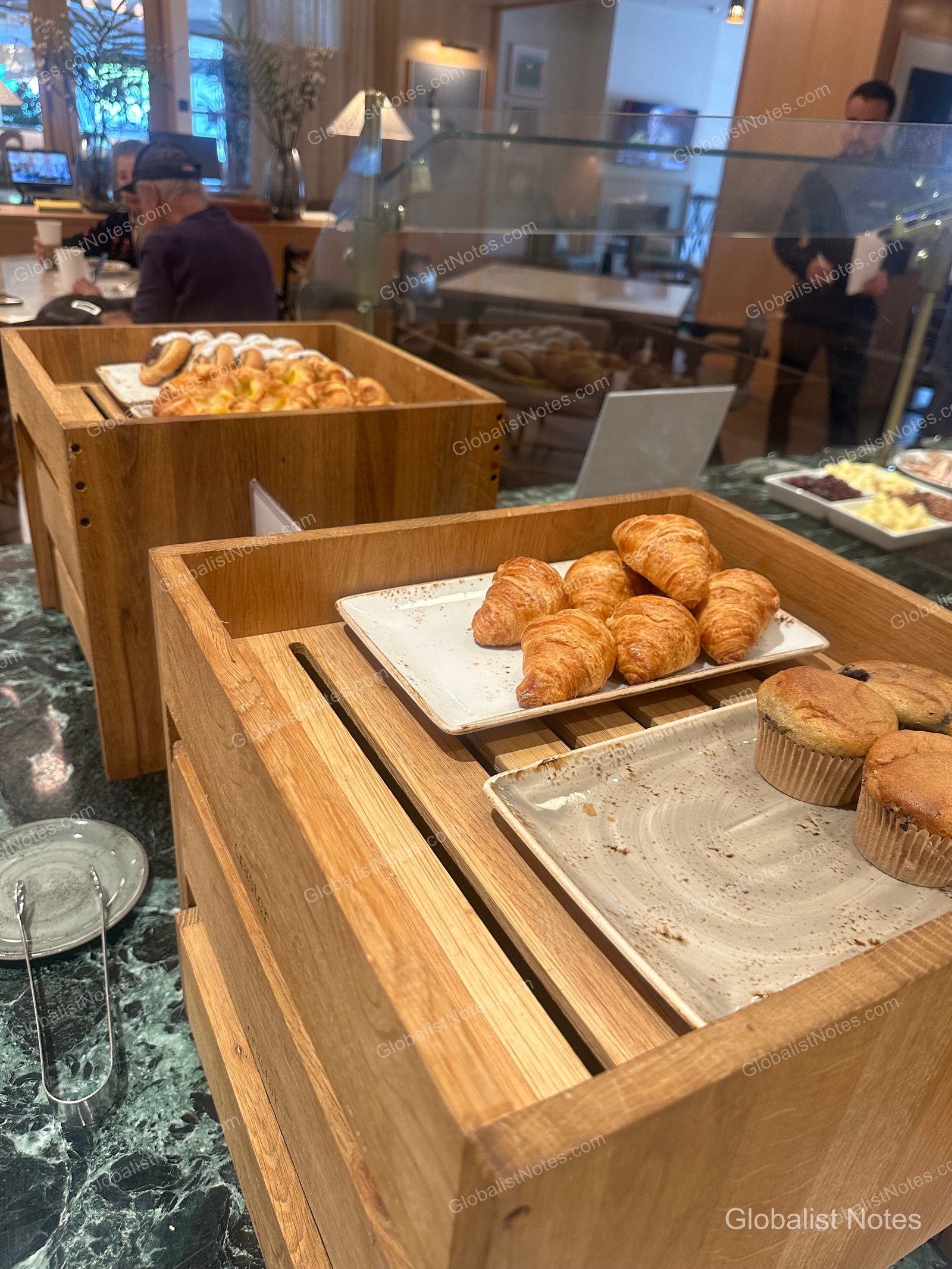 Hyatt Regency Irvine 自助早餐的烘焙區。木盒中擺放著裝有可頌與瑪芬的白色餐盤，背景隱約可見其他麵包種類及用餐房客。