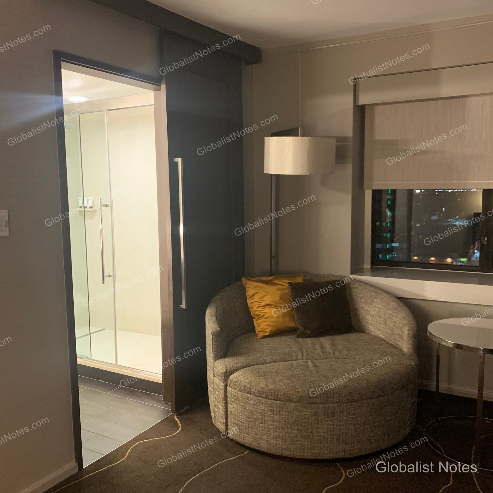 Grand Hyatt Denverの1キングベッド・コーナー・ルーム。窓際の円形ソファと、奥に見えるバスルームのガラス張りシャワーブースが照明に照らされている。