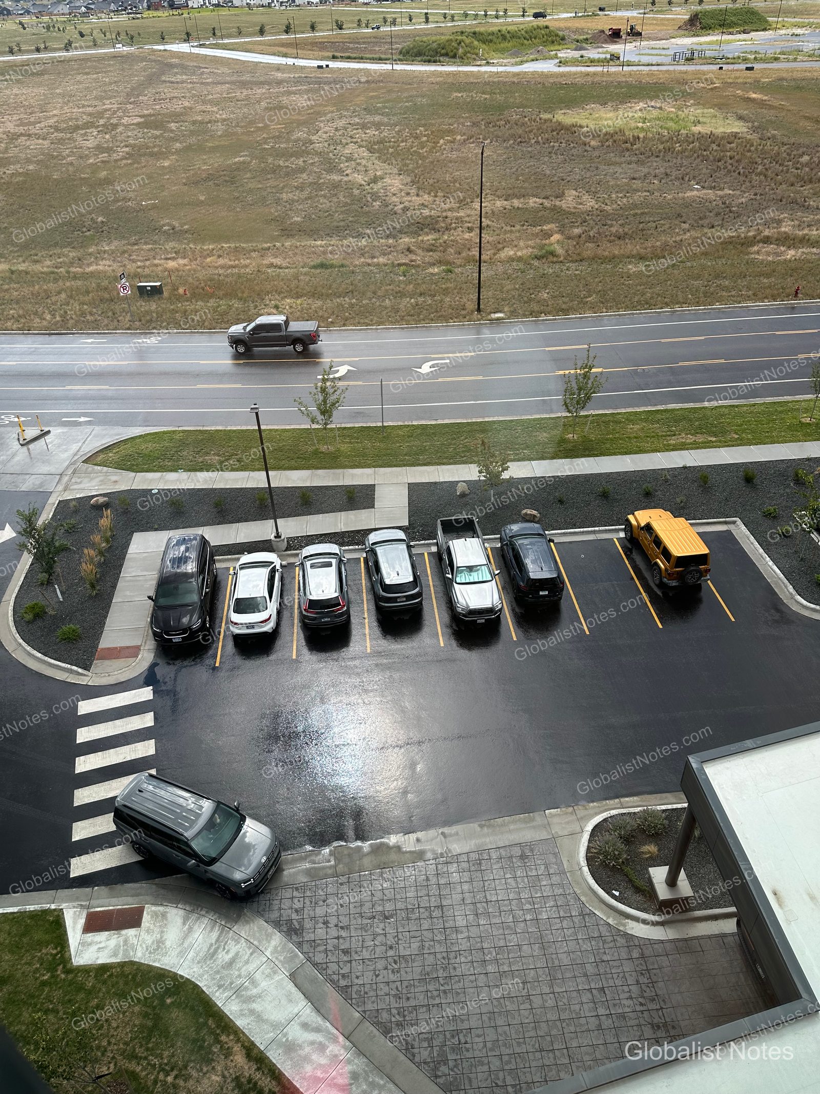 hyatt place Bozeman Yellowstone Airportの客室から見下ろした駐車場。濡れたアスファルトに数台の車が停まり、遠方には道路と広大な平原が広がっている。