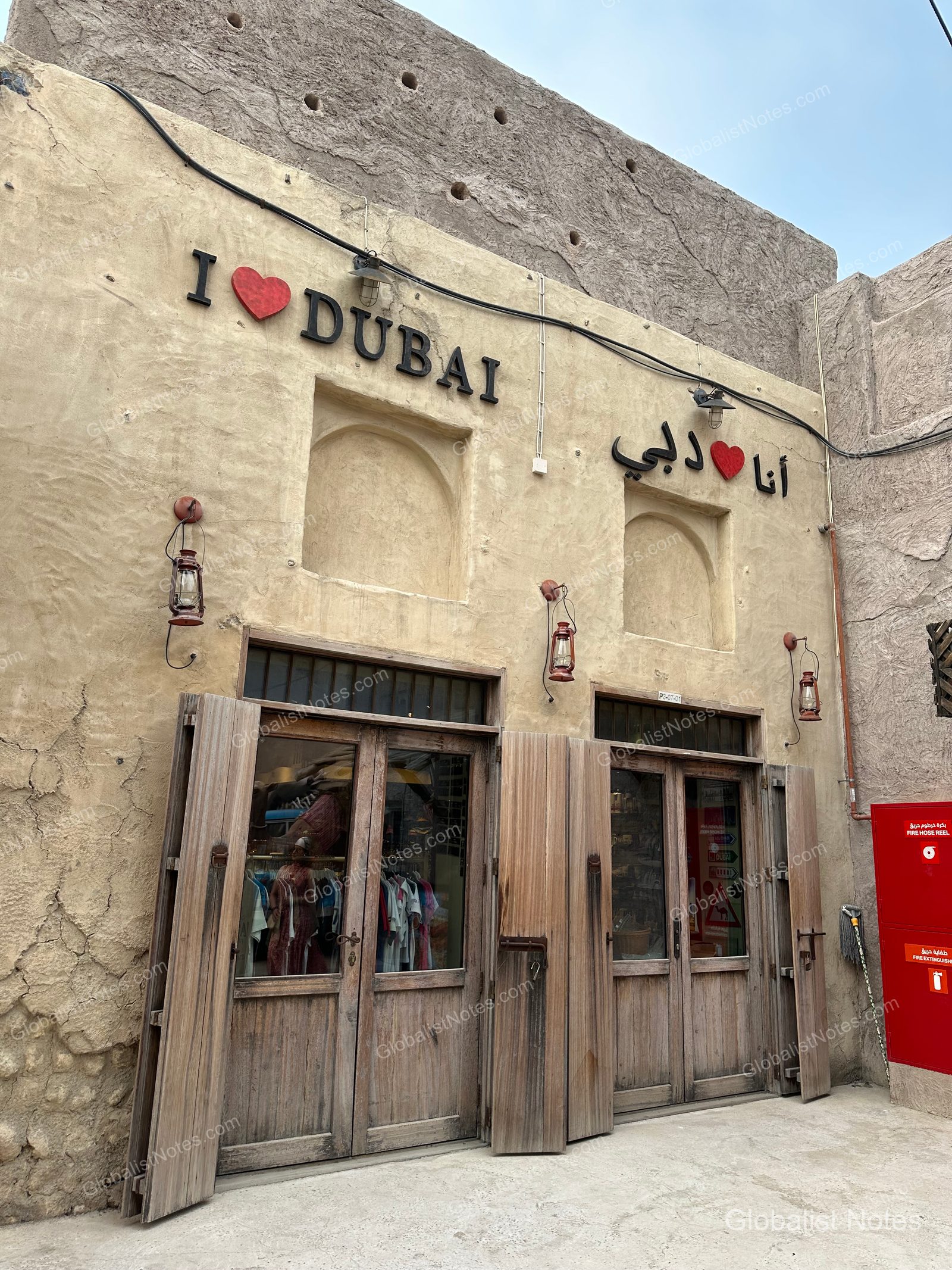 杜拜傳統土黃色建築外觀，牆面標示著「I LOVE DUBAI」的中英文與阿拉伯文標語，下方為木門商店入口。