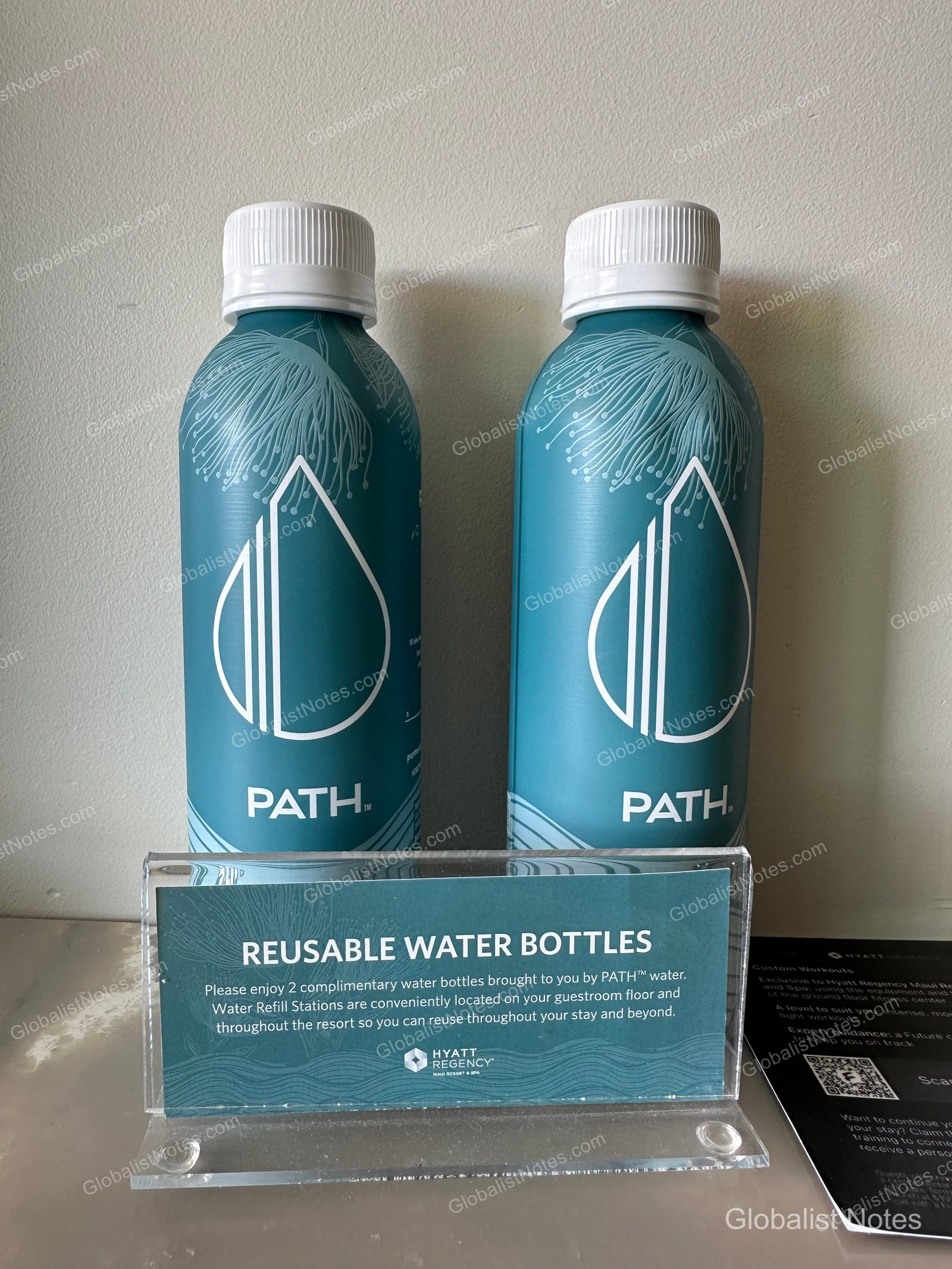 Two teal PATH reusable aluminum water bottles placed in a guest room at Hyatt Regency Maui Resort and Spa, with an instruction card in front explaining how to refill them at water stations throughout the resort.
