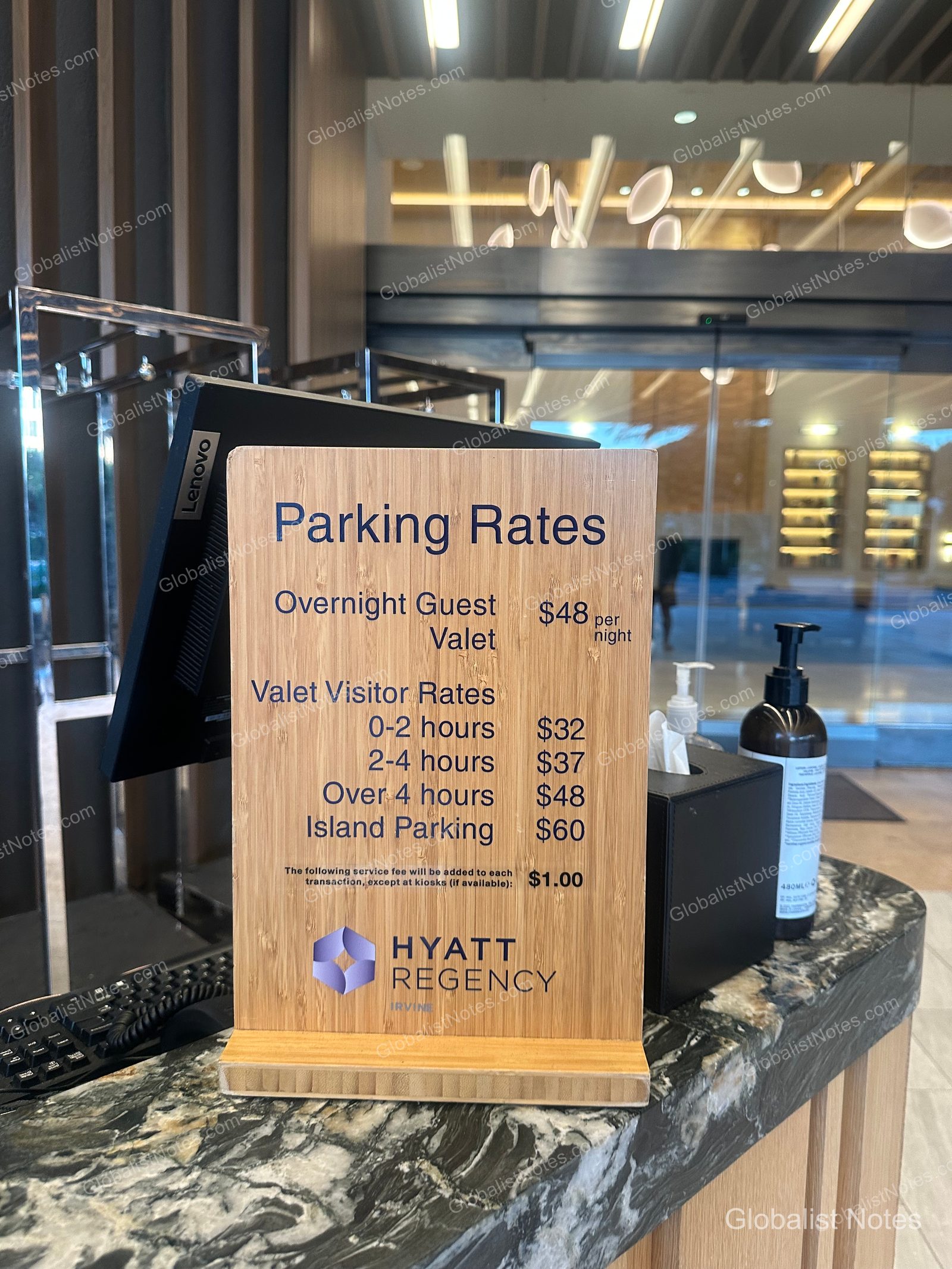 Hyatt Regency Irvine 前台的木質停車收費告示牌。住客代客泊車每晚 48 美元，並列有訪客時段收費及自助停車費用。