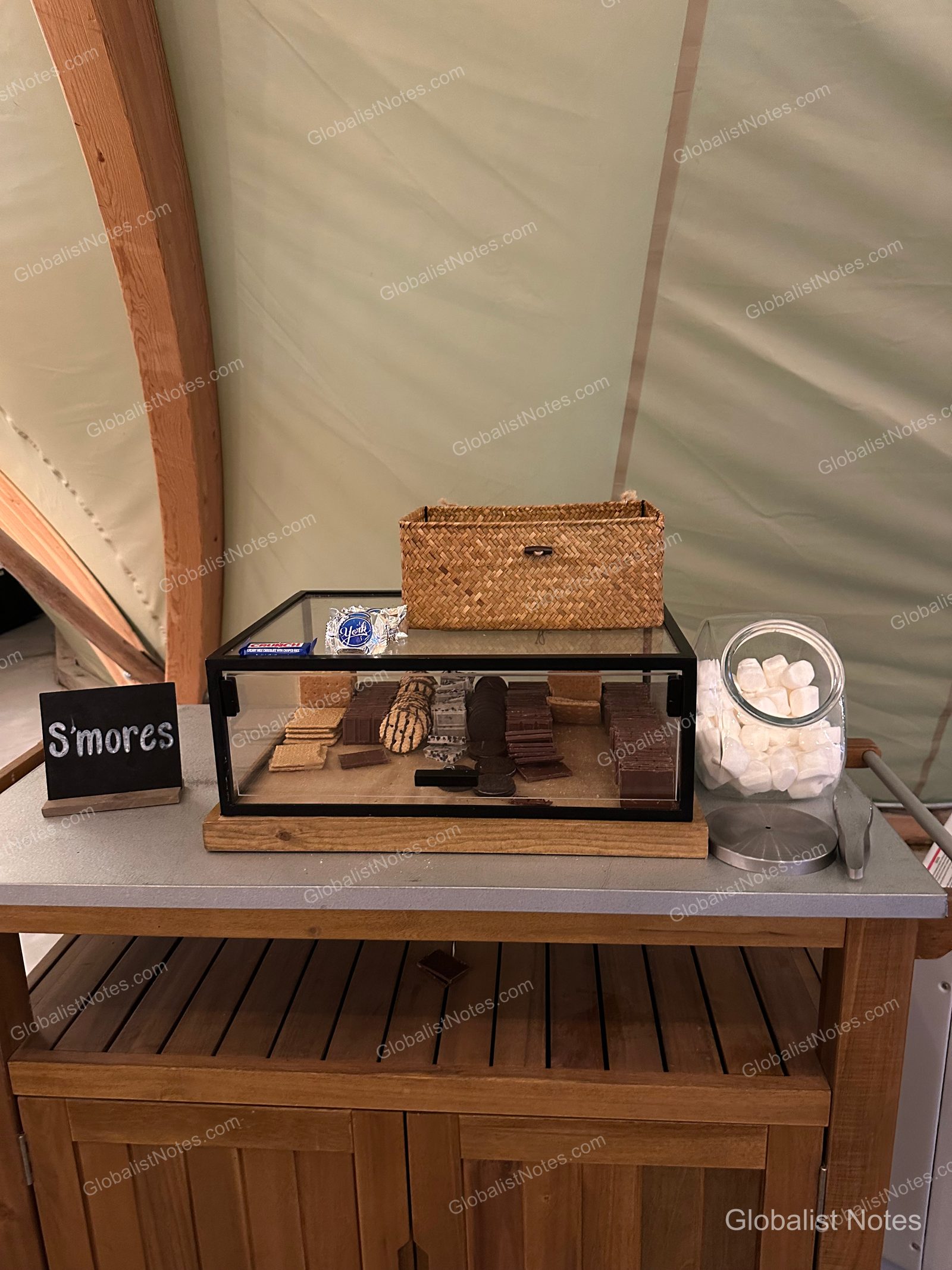 Under Canvas North Yellowstoneのテント内。木製テーブルの上に、クラッカー、チョコレート、マシュマロが入った瓶と「S'mores」と書かれた黒板が置かれています。
