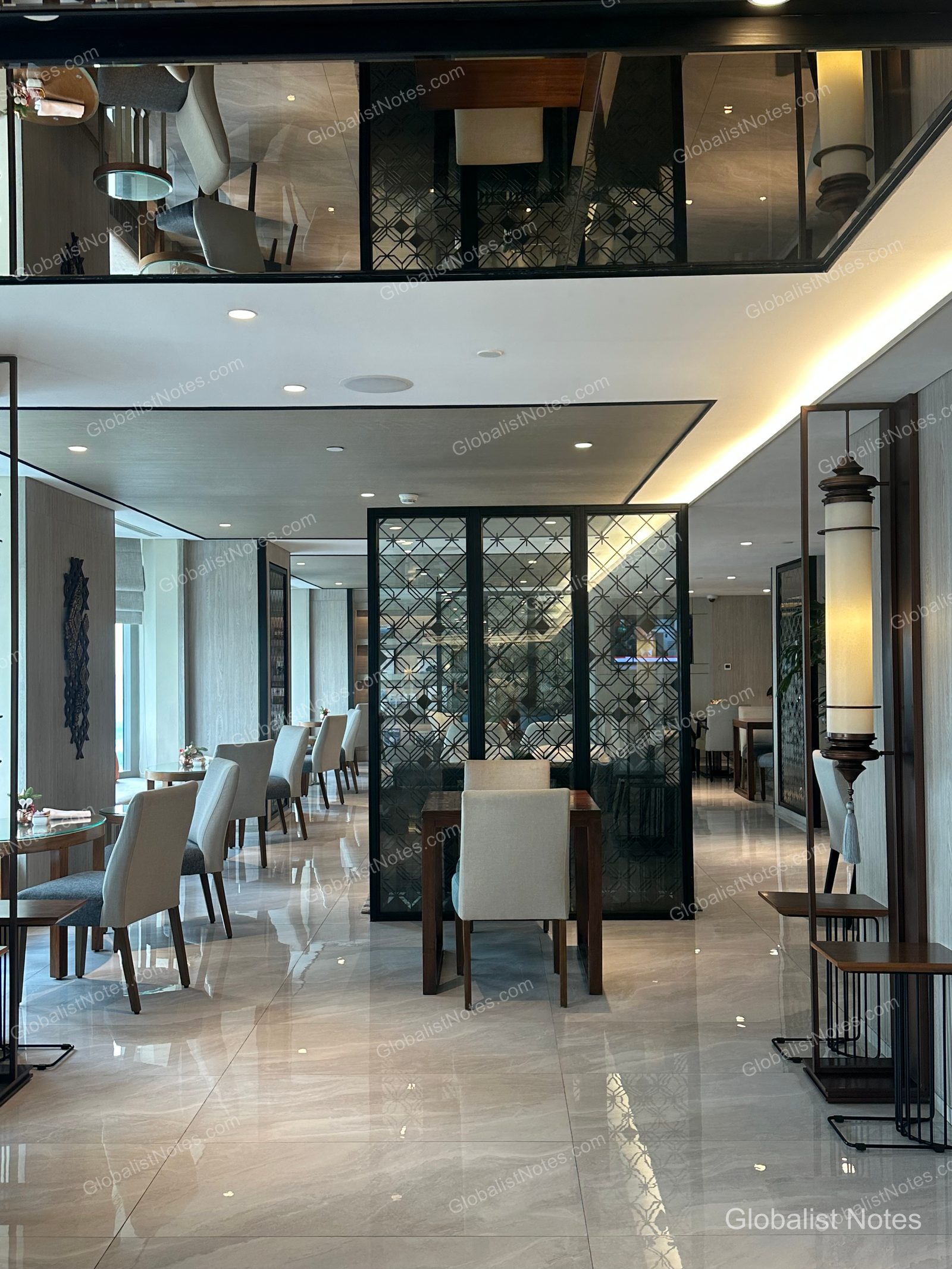 The interior of the Grand Hyatt Jakarta club lounge, featuring marble floors, modern lighting, and geometric partitions. Light beige chairs and wooden tables are neatly arranged, with mirrored ceiling accents that create a sense of spaciousness.