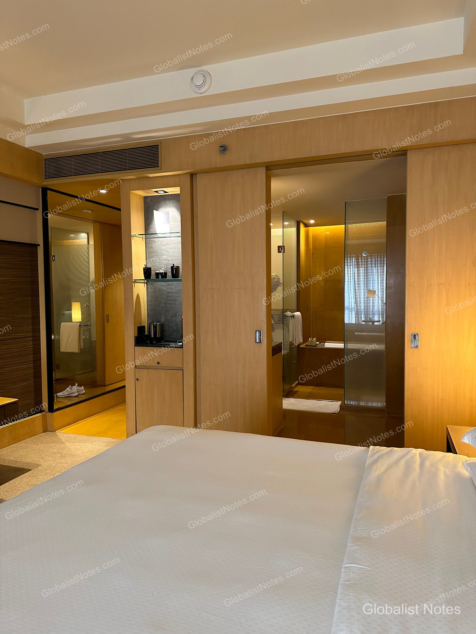 Interior view of the Veranda Suite King at Grand Hyatt Mumbai Hotel and Residences. The bathroom with sliding doors and the illuminated minibar are visible from the bed, set against a light wood-toned interior.