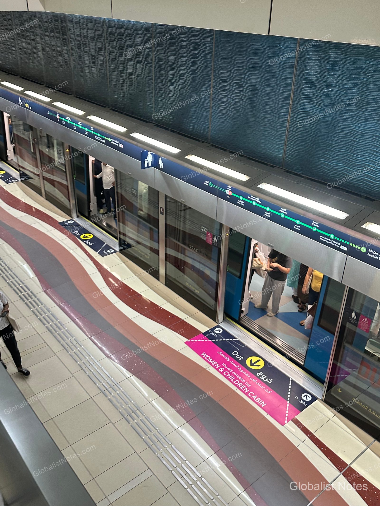 杜拜地鐵列車停靠於月台，車門開啟，地面標示著女性與兒童專用車廂的粉紅色圖示。