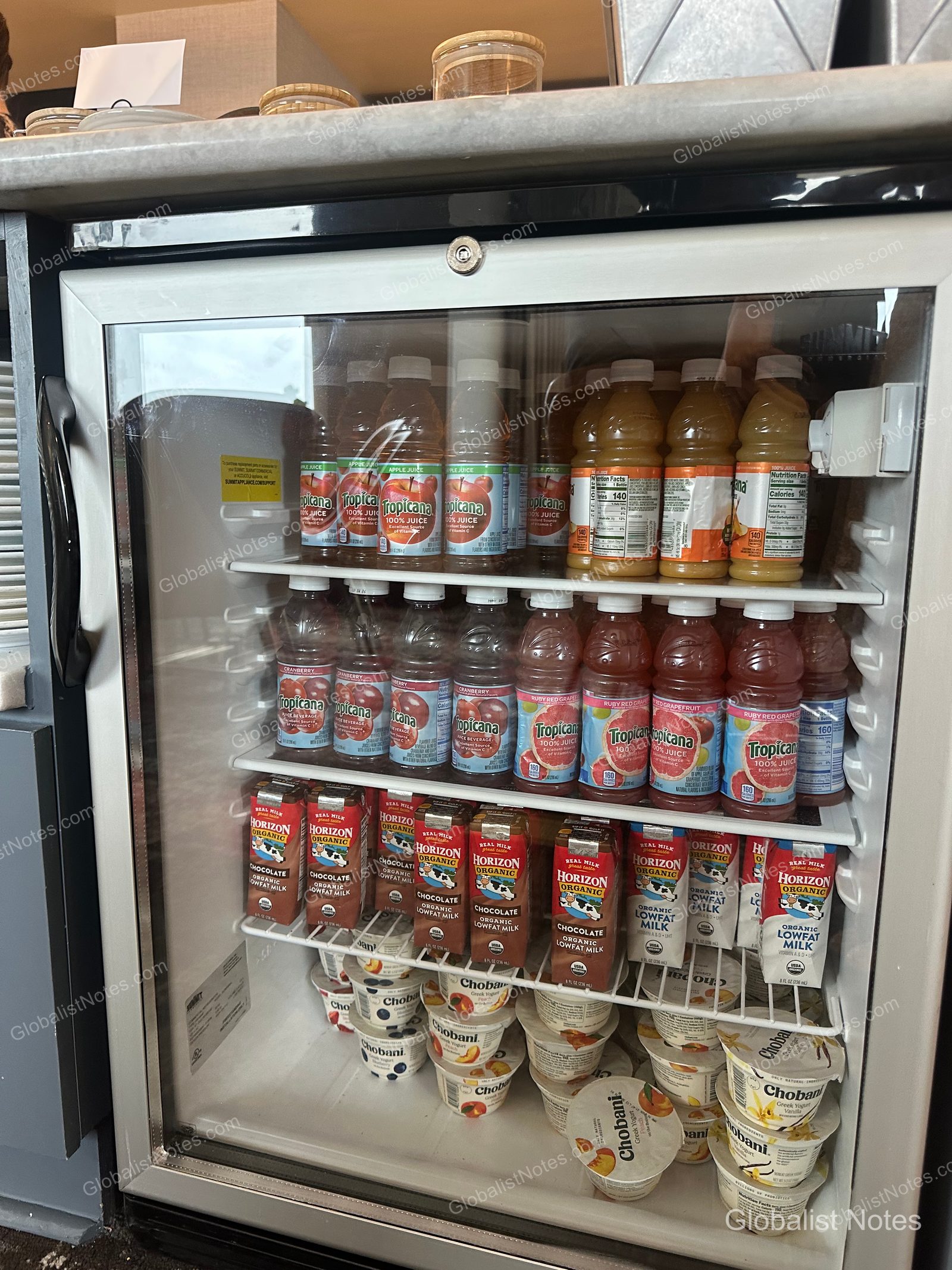 Glass refrigerators in the Grand Hyatt San Antonio River Walk breakfast area, neatly stocked with individual bottles of Tropicana juice, Horizon organic milk cartons, and various Chobani yogurts.