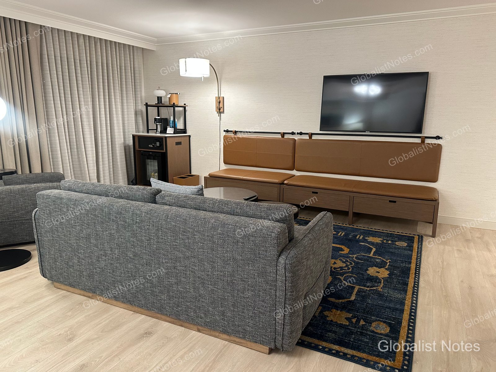 Hyatt Regency Irvine One-Bedroom Suite 的客廳，設有灰色沙發、牆面固定式棕色皮革長凳、壁掛電視，以及放置咖啡機的迷你吧。