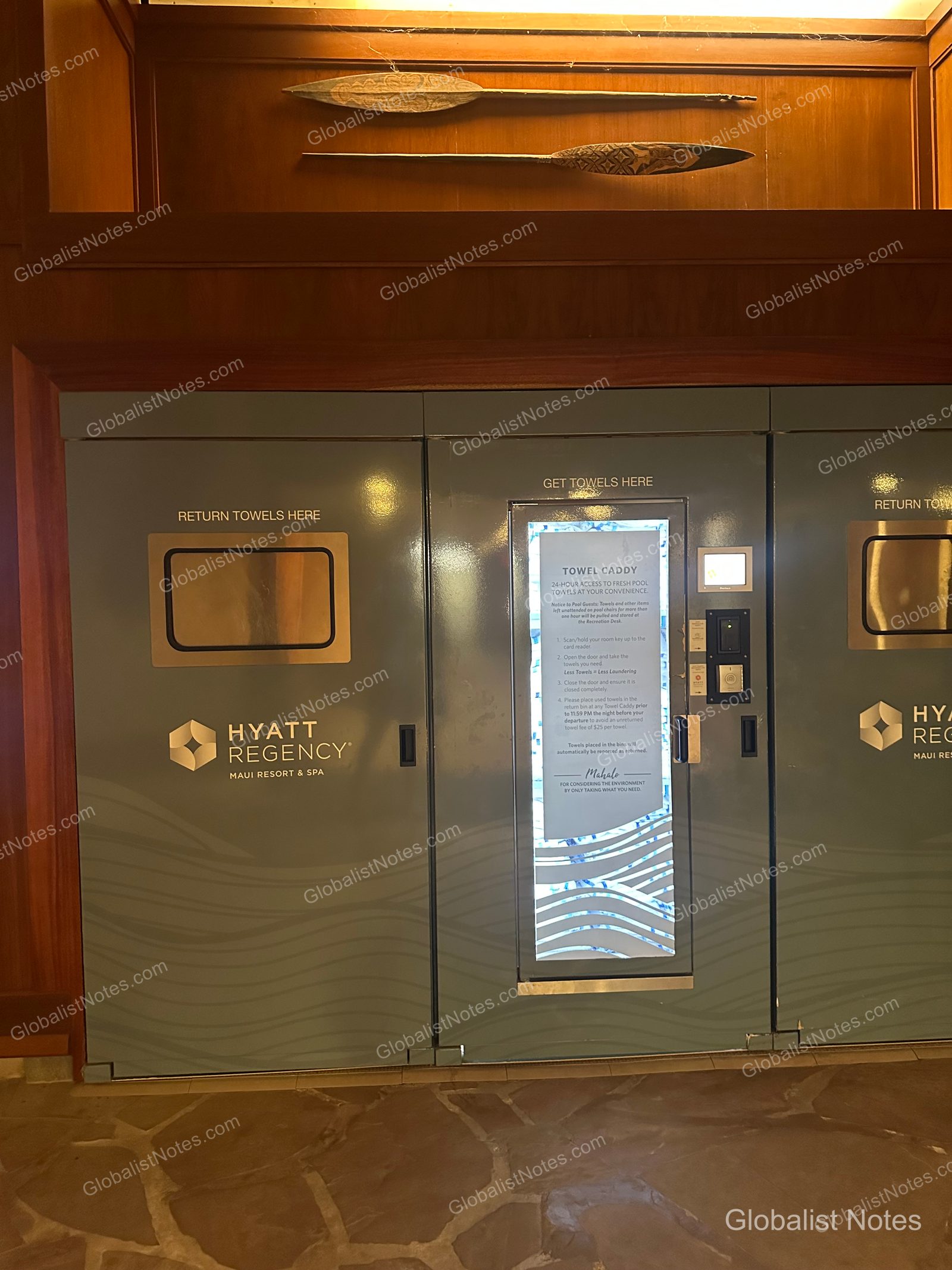 Towel caddy station at Hyatt Regency Maui Resort and Spa. The center features a kiosk where guests scan their room key to check out towels, with drop-off slots for used towels on either side. Two traditional wooden window frames are mounted on the wall above.