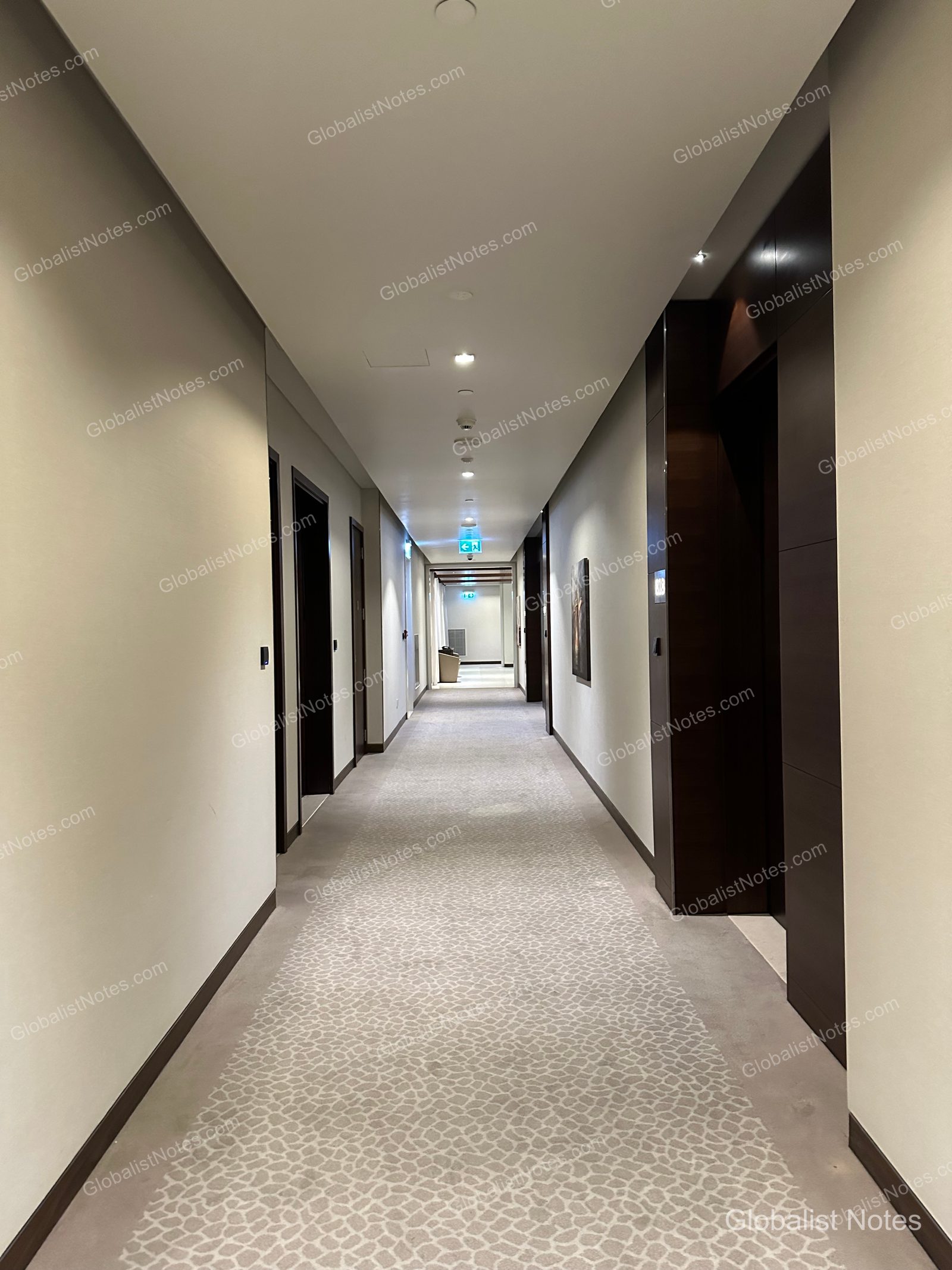 Hyatt Place Dubai Wasl District 客房走廊。淺米色牆面與深褐色房門形成對比，地面鋪設幾何圖案地毯，天花板設有一排嵌入式照明。
