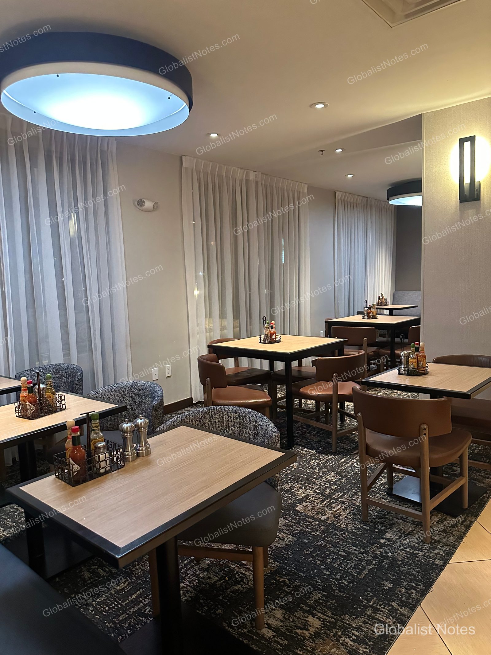 Hyatt Place El Paso Airport 的早餐區，設有多張方形餐桌，搭配棕色皮革椅與灰色布面座椅。桌上備有醬料與調味品，窗邊掛著白色窗簾，地面鋪設幾何圖案地毯。