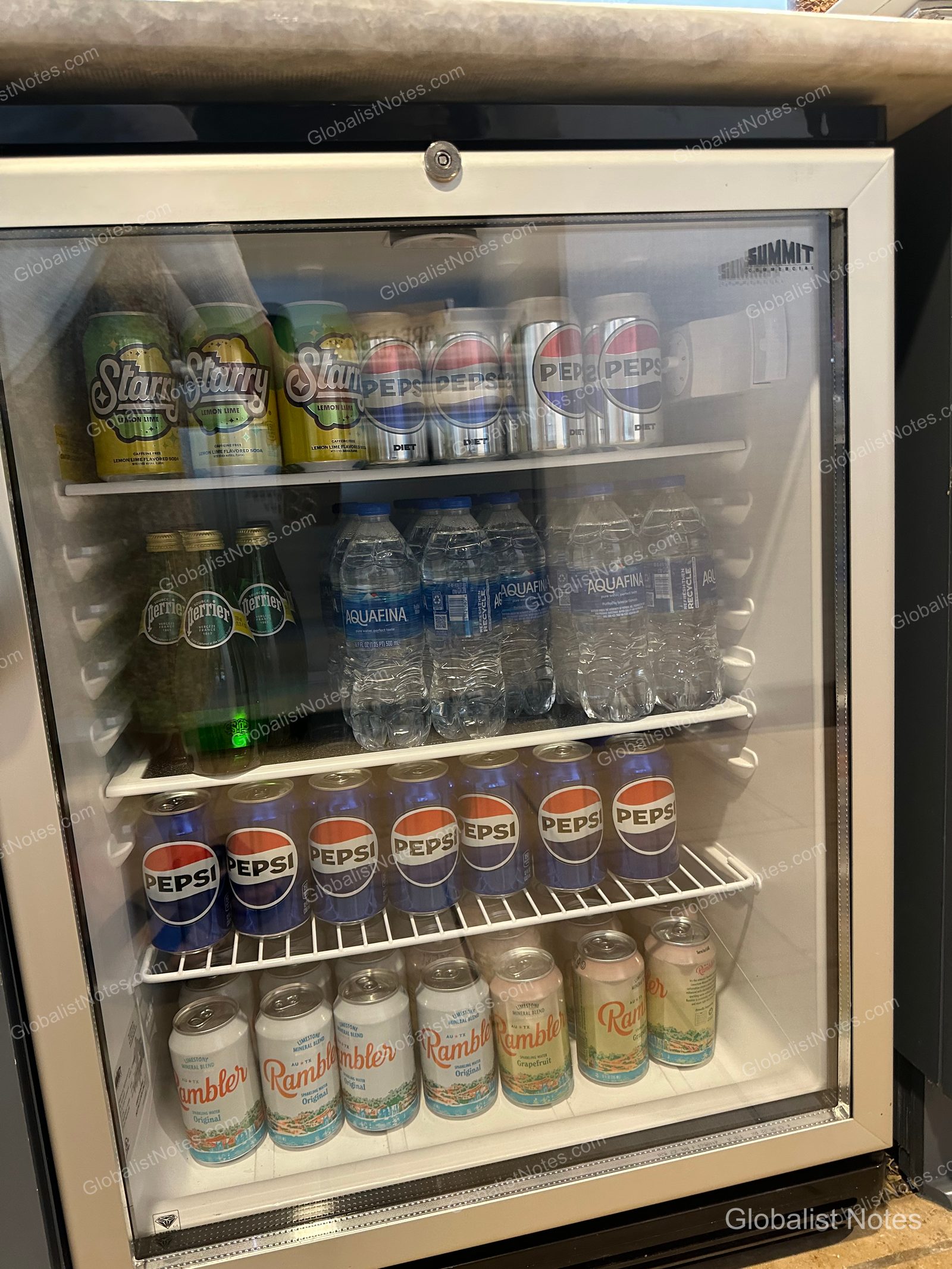 The interior of the minibar fridge in an Executive Suite at Grand Hyatt San Antonio River Walk, stocked with Starry, Pepsi, Diet Pepsi, Perrier, Aquafina, and Rambler sparkling water on four shelves.