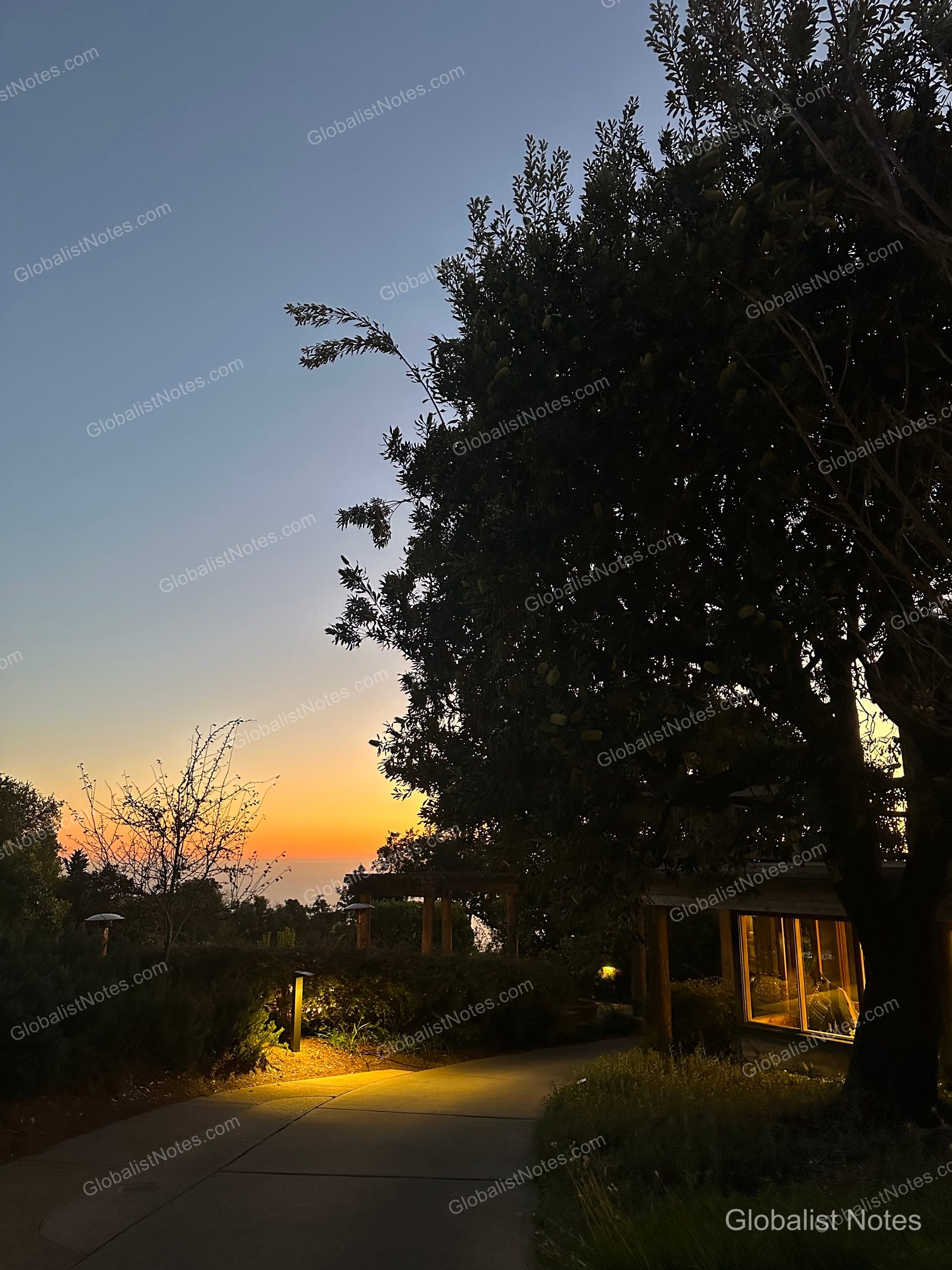 Sunset at Alila Ventana Big Sur, with an orange glow on the horizon, illuminated pathways, and tree silhouettes.