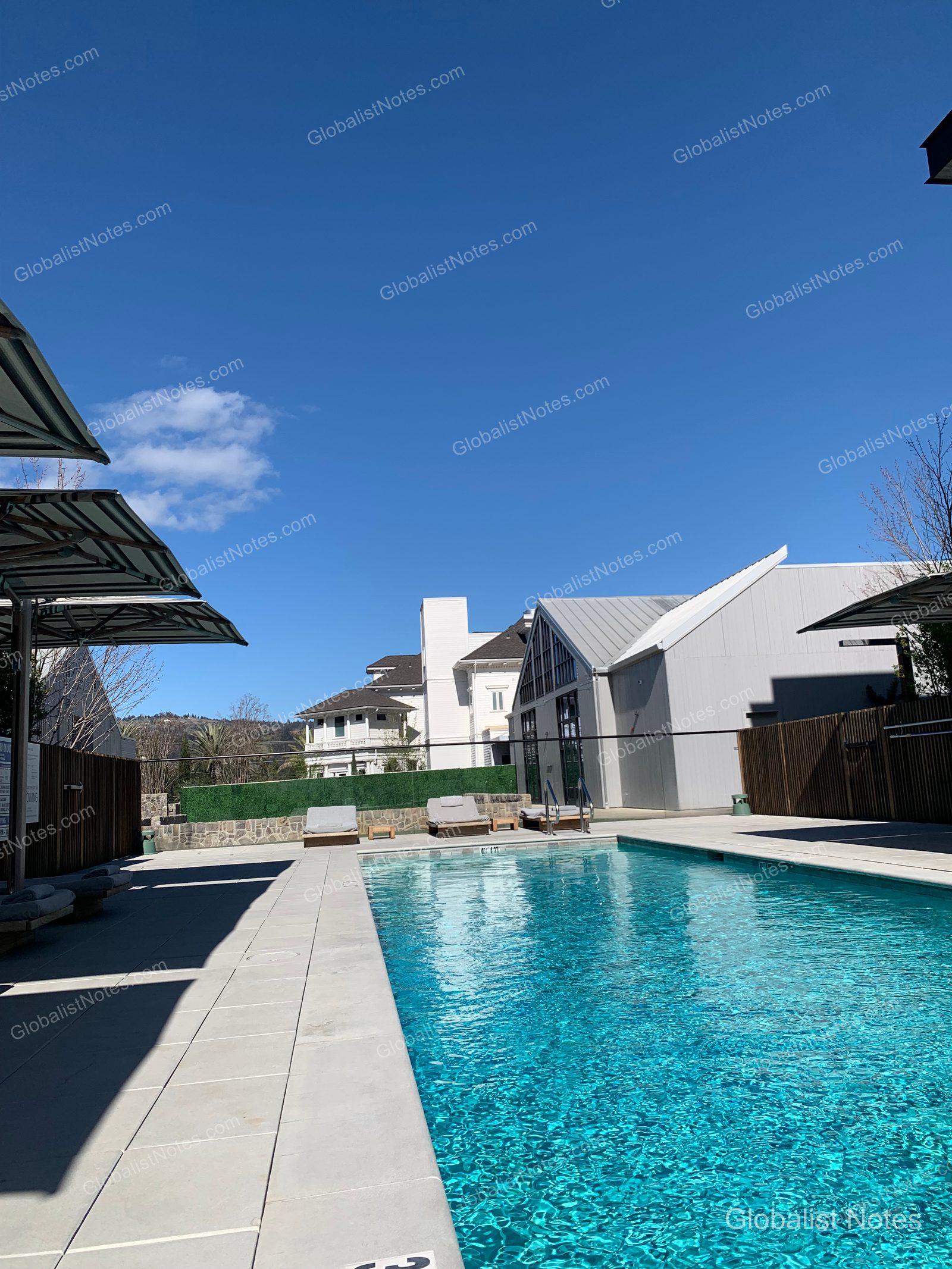 Outdoor pool view at Alila Napa Valley in St. Helena, USA. The rectangular pool is filled with blue water and surrounded by modern architecture and sun loungers, creating a neat relaxation area under a clear sky.