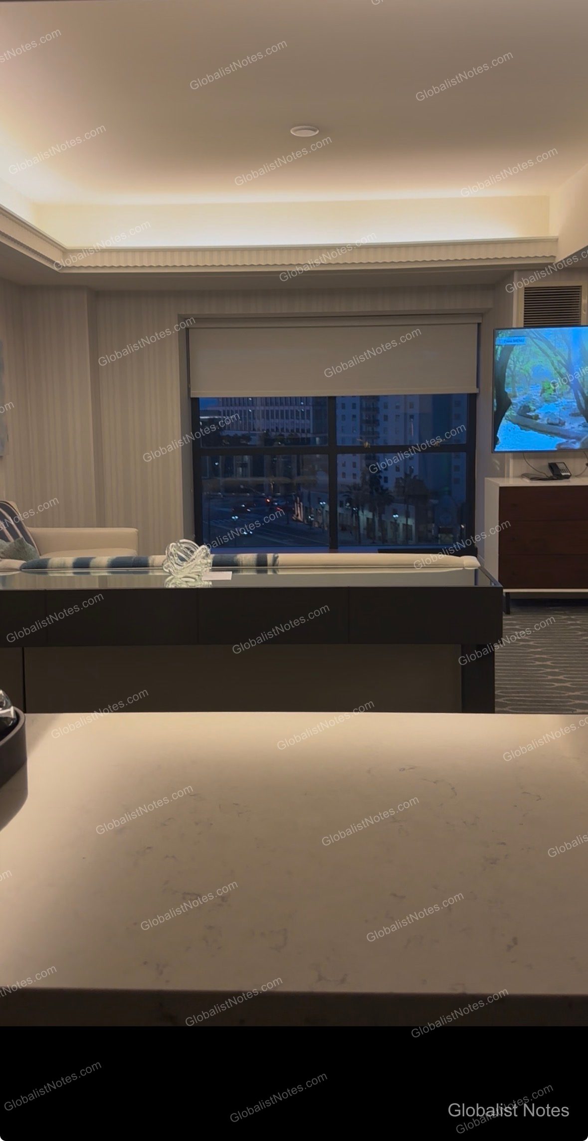 Manchester Grand Hyatt San Diego 1 King Bed Studio Deluxe 房型內部。前方為明亮的大理石桌面，後方設有沙發、可眺望聖地牙哥市區夜景的窗戶，以及壁掛式電視。