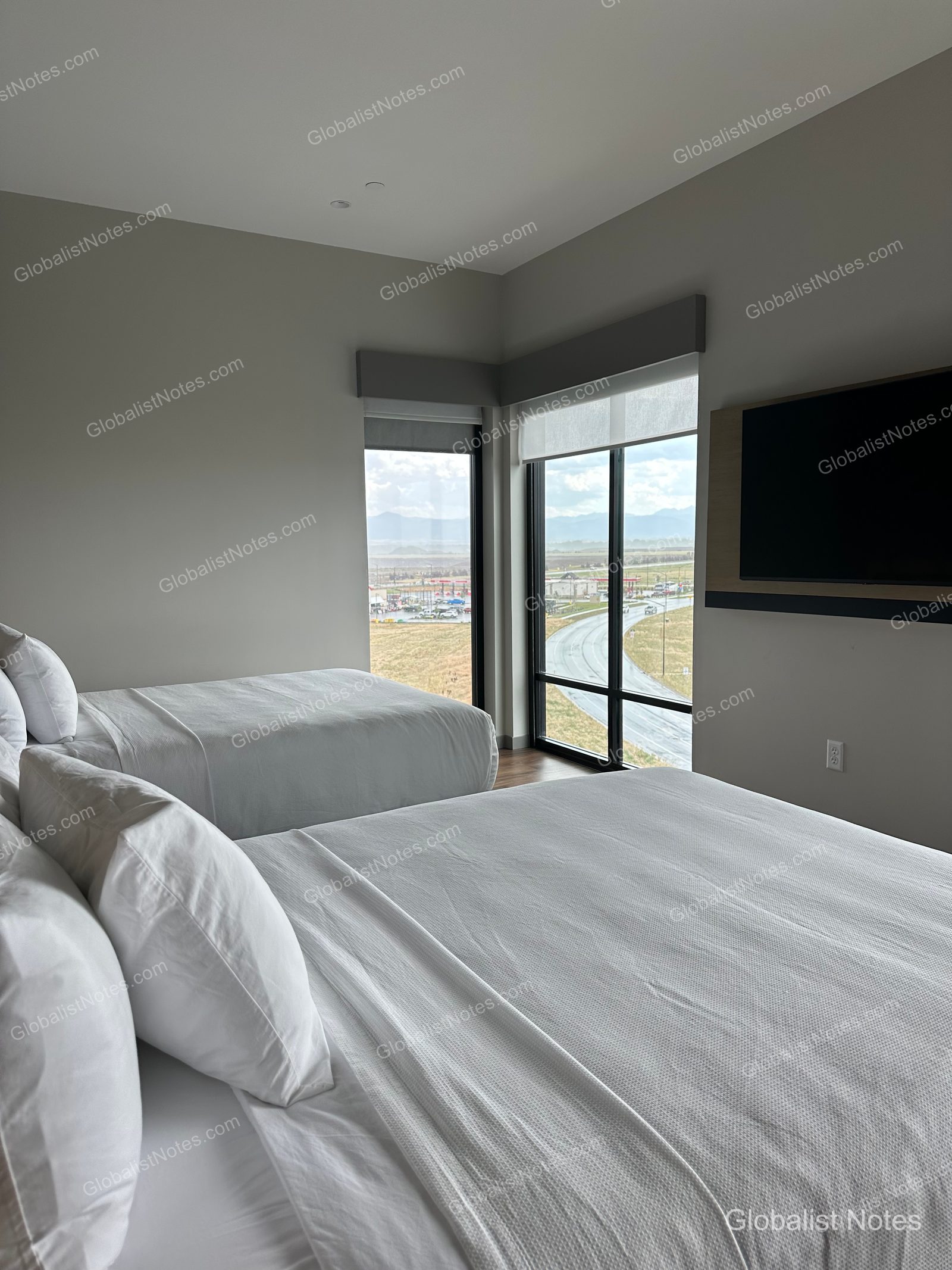hyatt place Bozeman Yellowstone Airportのジュニアスイート内部。白い寝具のベッド2台と壁掛けテレビがあり、窓からは空港近くの道路と開けた景色が見渡せる。