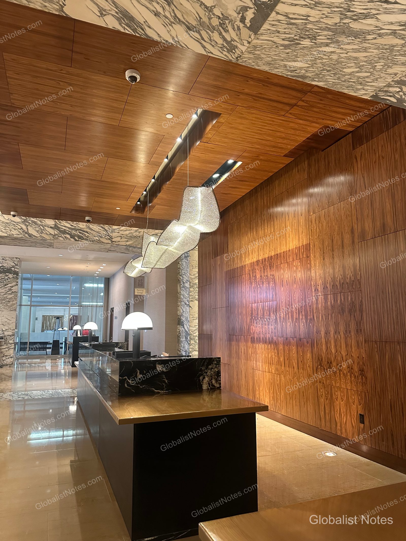 The check-in desk at Grand Hyatt San Antonio River Walk, featuring black marble and metal countertops, unique pendant lighting, and warm-toned wood paneling on the walls.