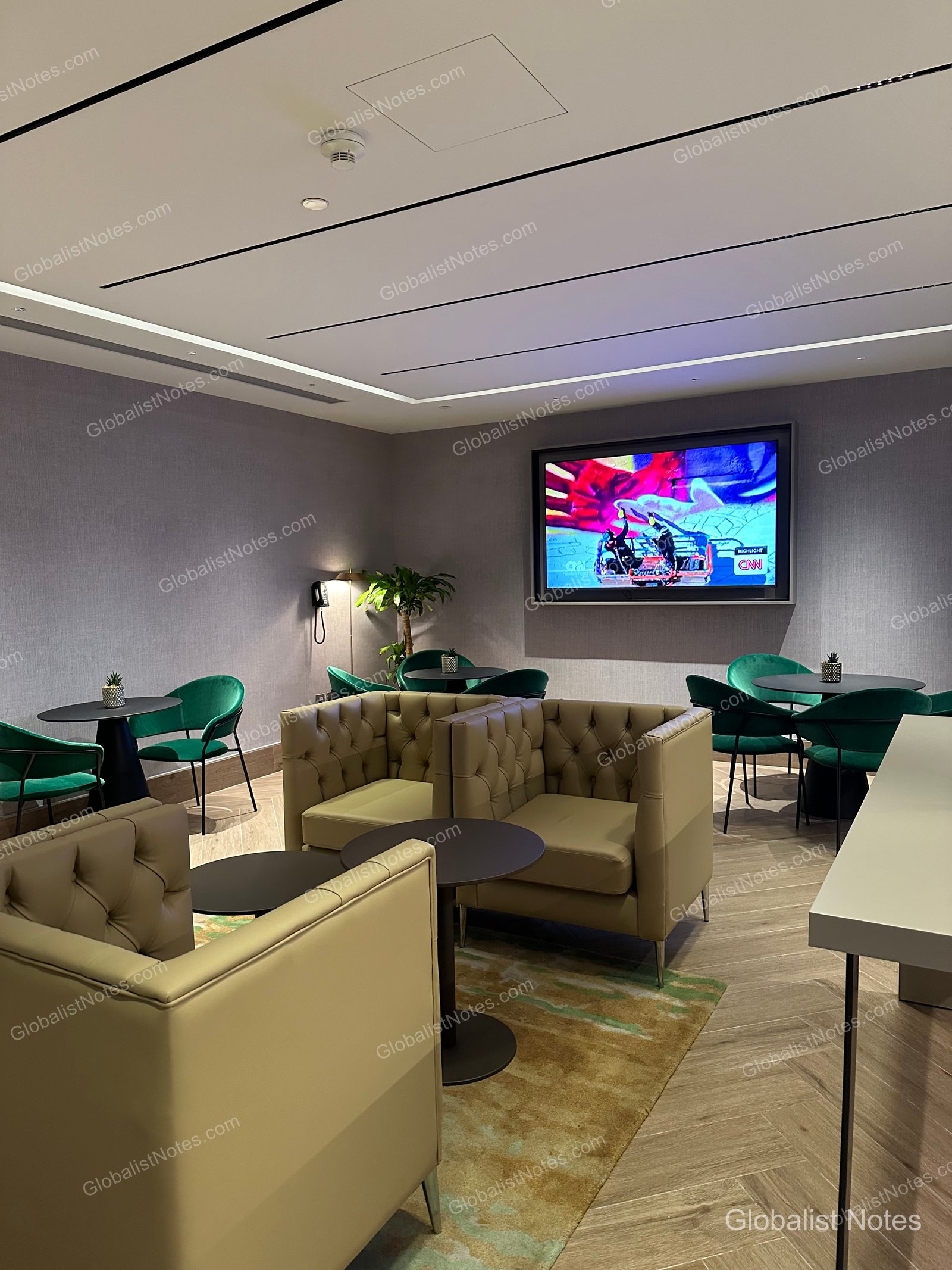 The lounge area at Hyatt Regency Malta, featuring beige leather armchairs, dark green velvet seating, and a wall-mounted TV, all set against patterned carpeting.