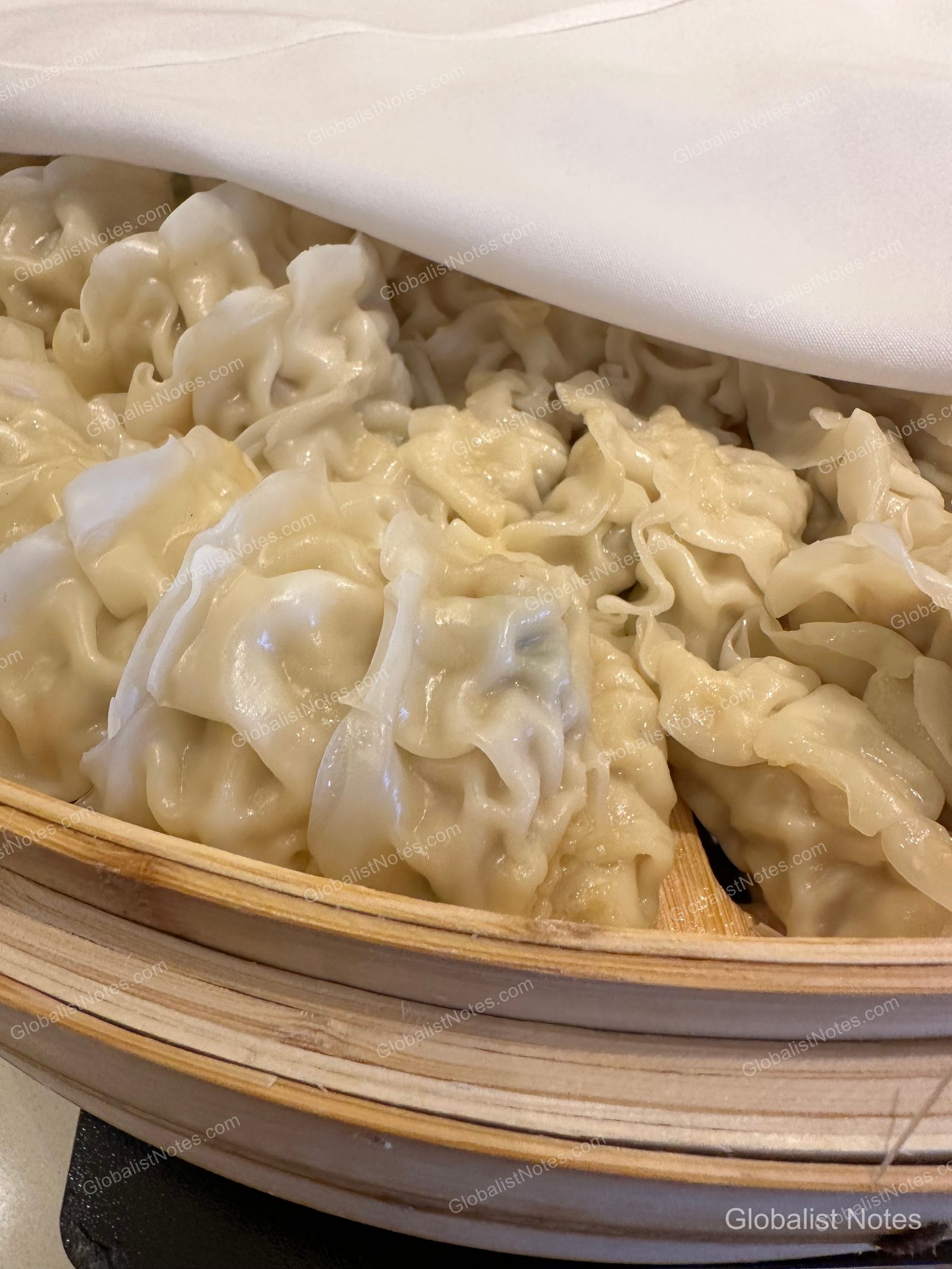 Freshly steamed dumplings served in a bamboo steamer, partially covered with a white cloth.